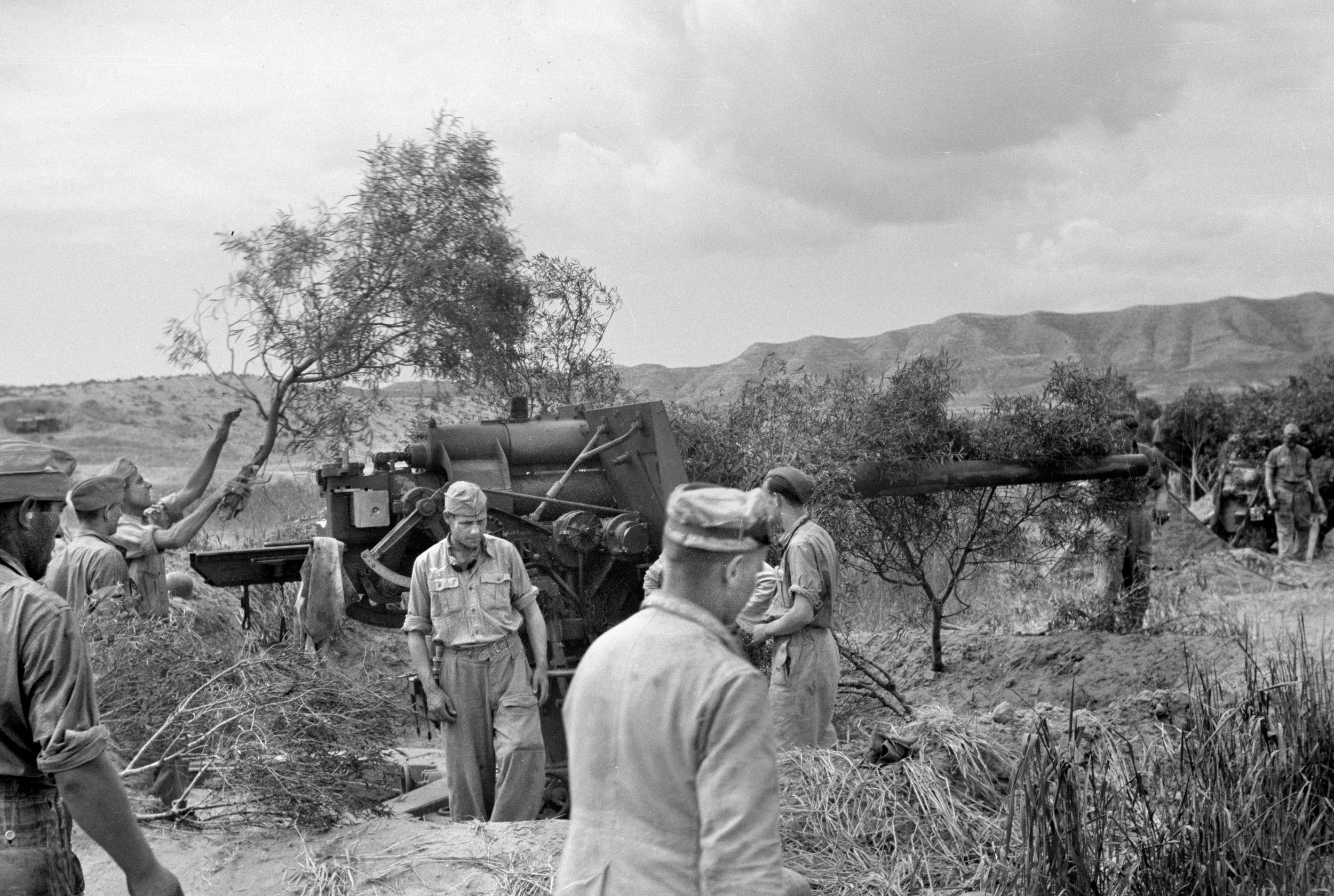 German soldiers camouflage an 88mm gun in the desert. The 88 was originally a flak gun but proved deadly against Allied armor in North Africa where Ernest Hollands and his Churchill tank narrowly avoided destruction from two of them in a matter of minutes.