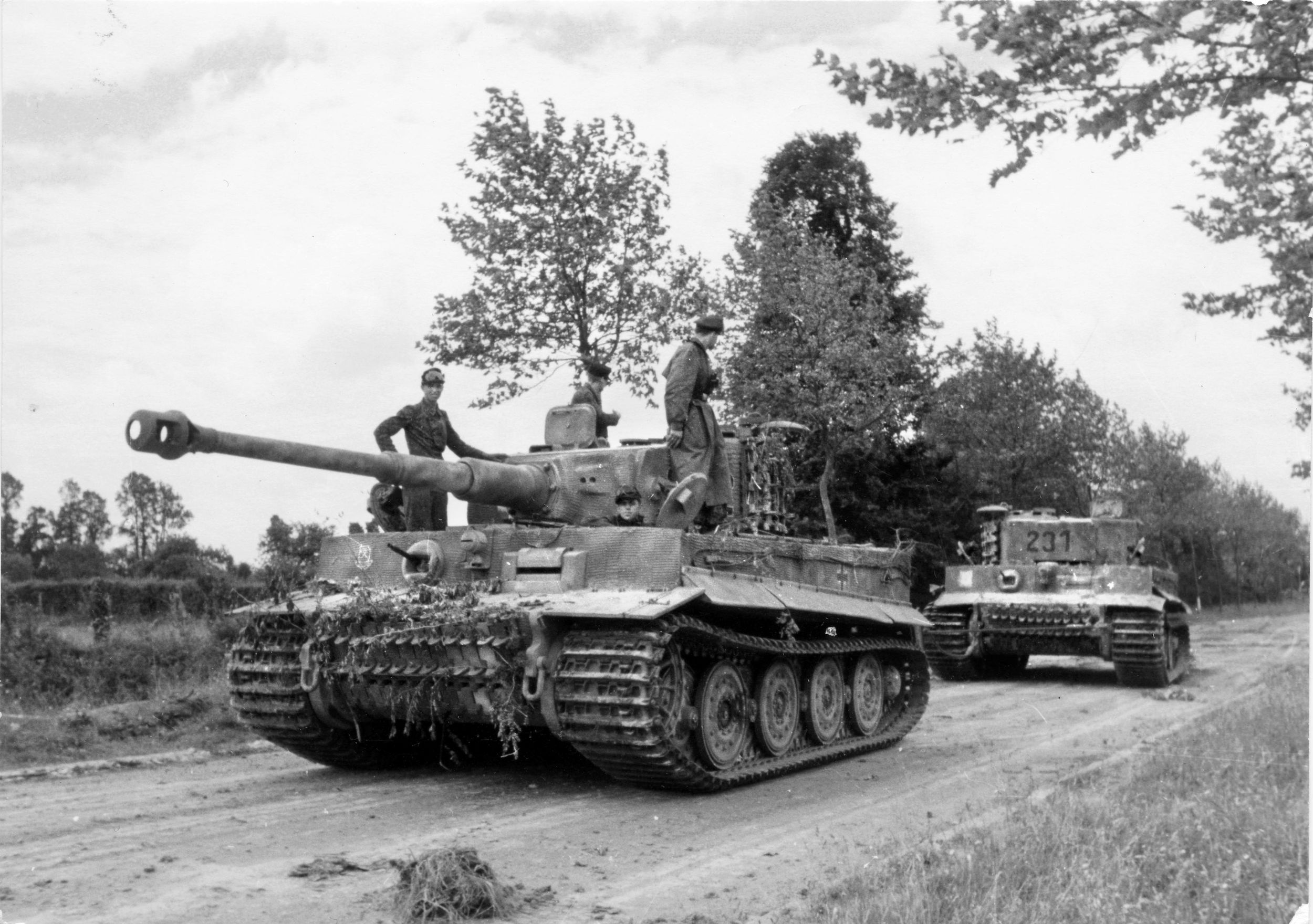 The crew of a German Tiger tank; pulls a damaged Tiger away from the scene of the fighting at Villers-Bocage. German armored units were usually forbidden from executing recovery operations like this due to Allied air superiority, and the crewmen on top of the tank may be watching for Allied fighter bombers.