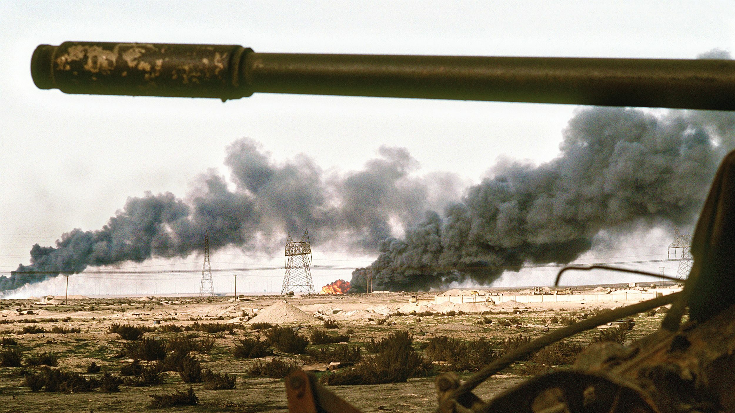 Thick black smoke seen in the distance beyond a burned-out Iraqi tank streams skyward after Iraqi forces withdrawing from Kuwait set fire to the Arab emirate’s oil fields.