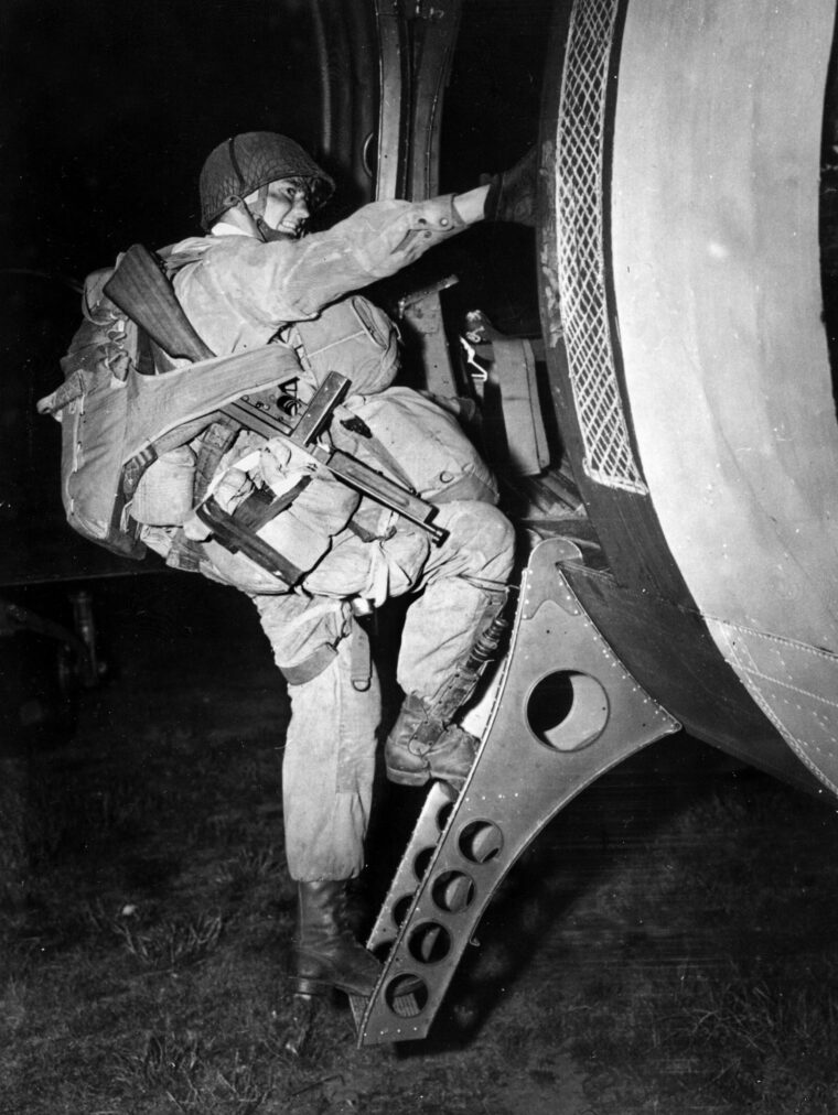 T/4 Joseph Gorenc, a heavily laden paratrooper with HQ Company, 3rd Battalion, 506 Parachute Infantry Regiment, 101st Airborne Division, flashes a confident smile as he hoists himself into one of hundreds of C-47 "Skytrain" transport aircraft that were used to carry troops and gliders to Normandy on the night of June 5-6 1944.