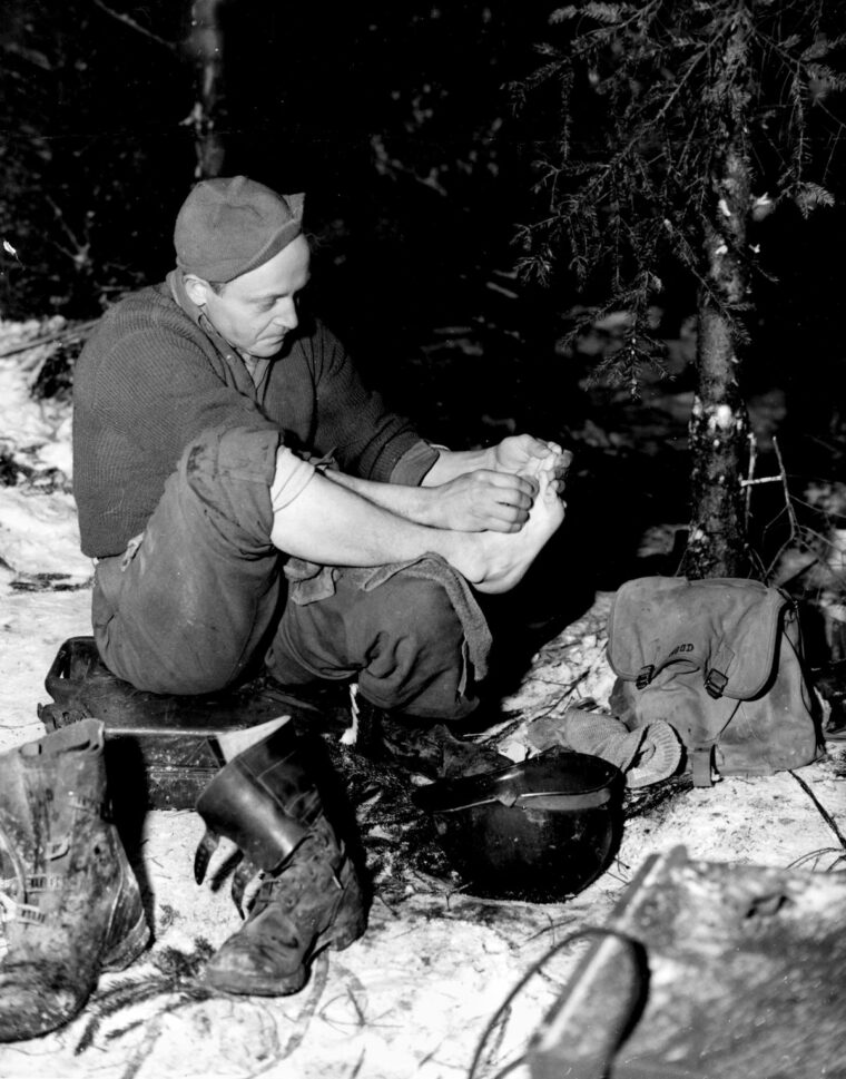 Keeping feet clean and dry was essential for preventing trench foot and frostbite. Here Corporal Lloyd Hood of the 101st takes advantage of a lull in the fighting for personal maintenance. 