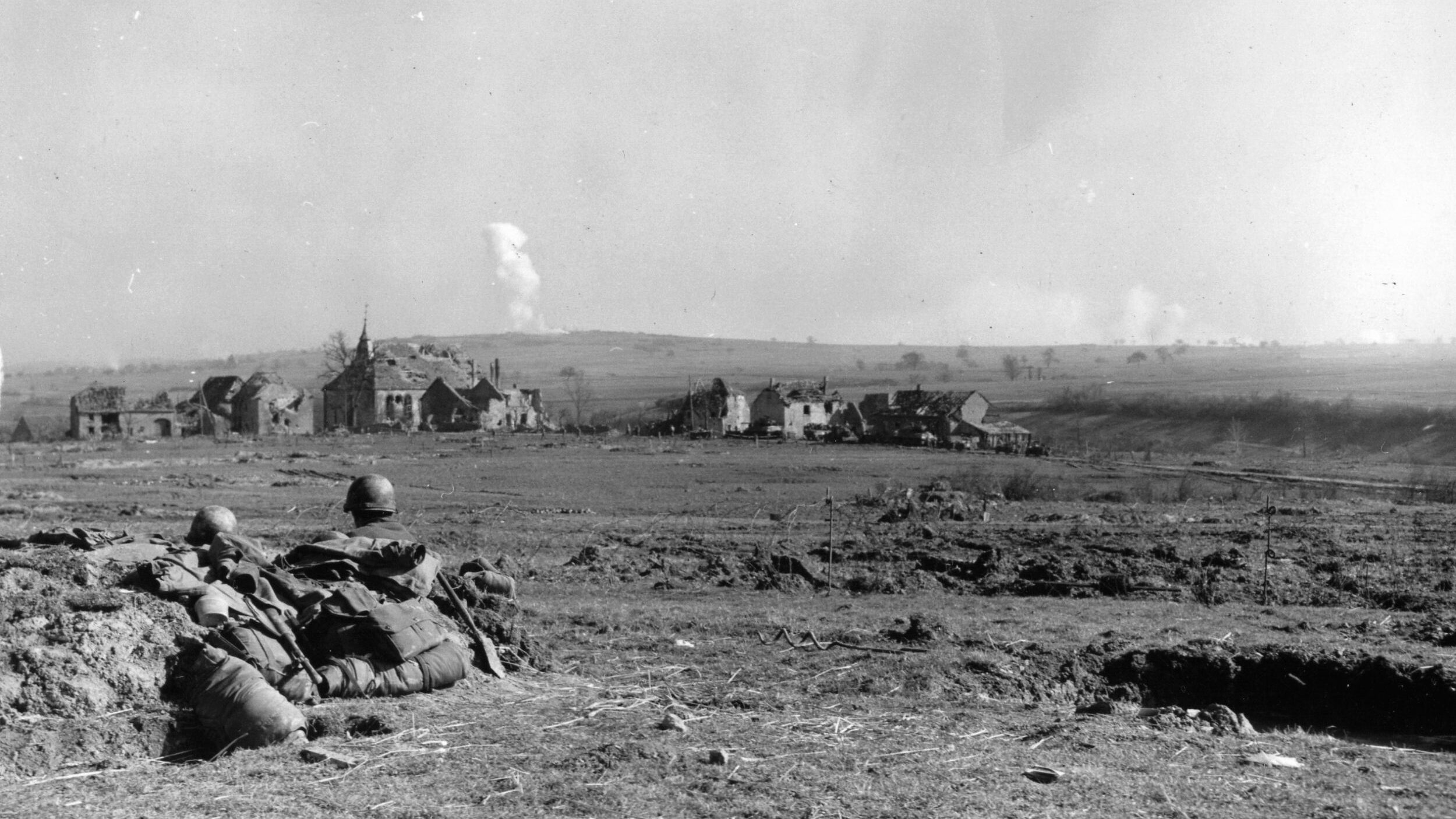 A safe distance away, two soldiers of the U.S. 44th Division observe the shelling and aerial bombardment of German positions near the village of Enchenberg. German tanks harassed American infantry throughout their fight for the town.