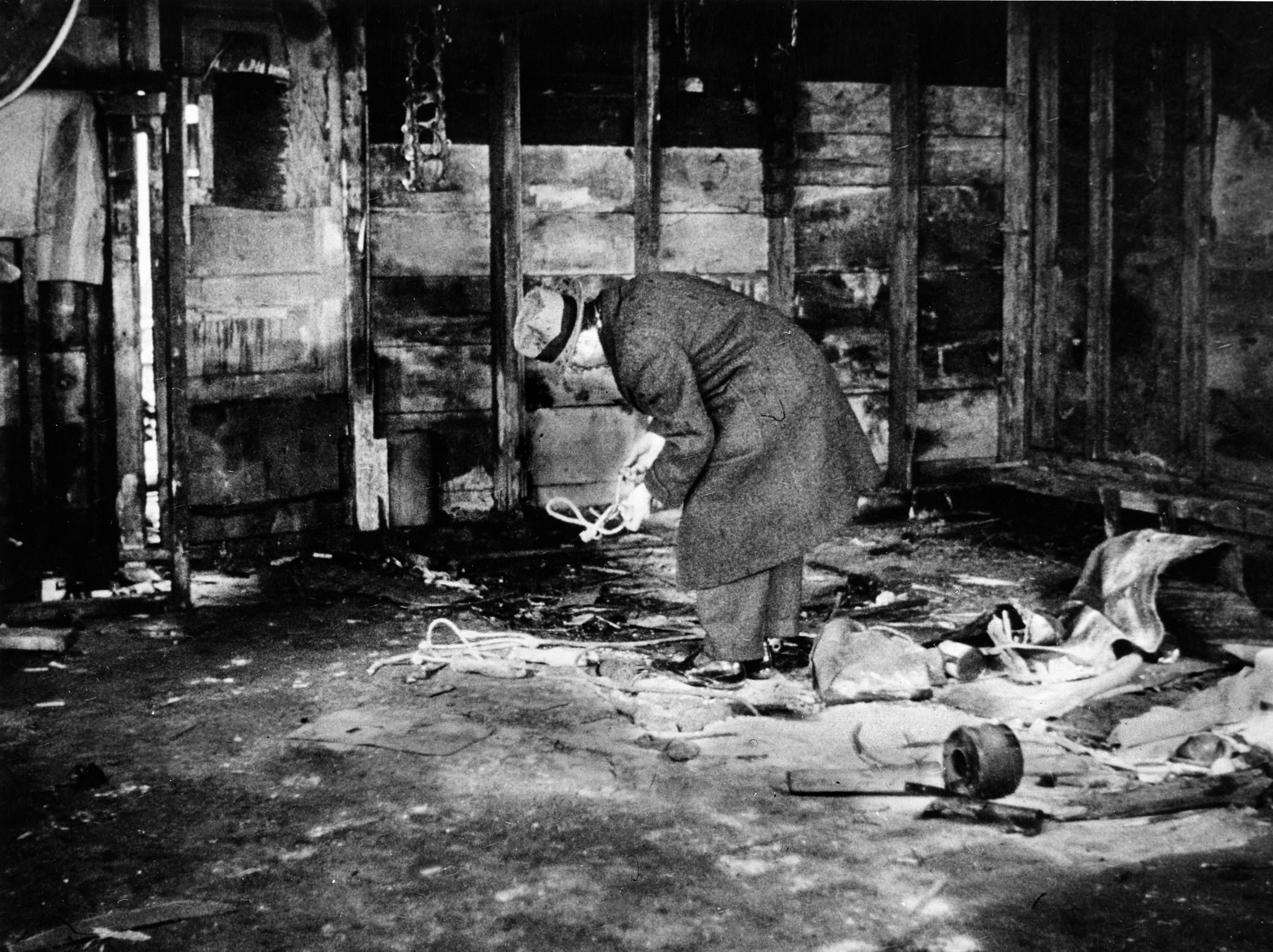 An inspector looks at evidence of a Black Market meat operation in a filthy building. The black marketeers spread lime on the floor in a poor attempt at cleanliness. 