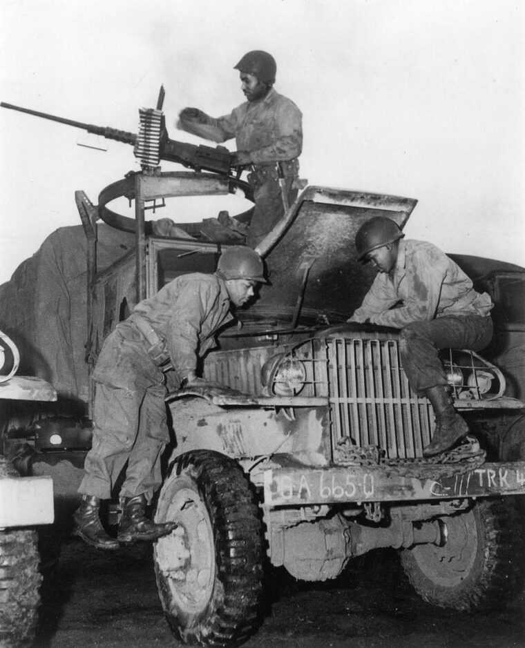 African American members of the Red Ball Express repair a 25-ton truck while a crewman keeps a watchful eye for the enemy. 