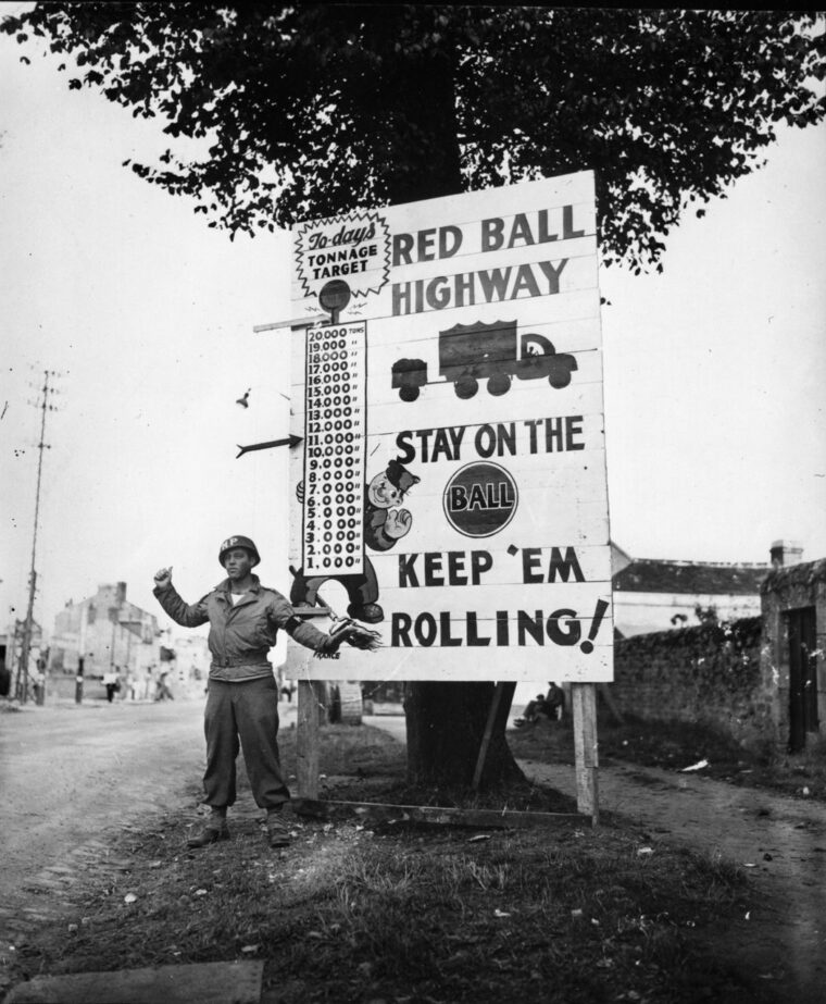 A corporal in the 783rd Military Police Battalion waves a Red Ball convoy through on its way to forward areas near Alençon, France, September 5, 1944.