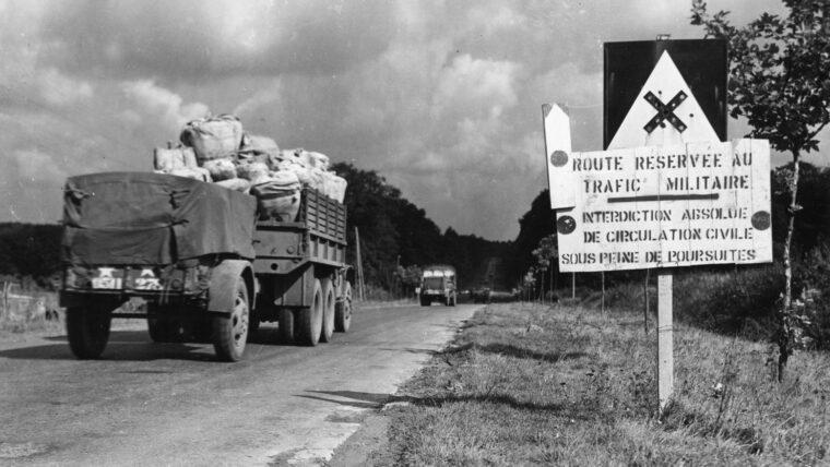 Trucks and trailers loaded with supplies pass a sign warning civilian traffic to stay off the express route reserved for Red Ball Express and military use.