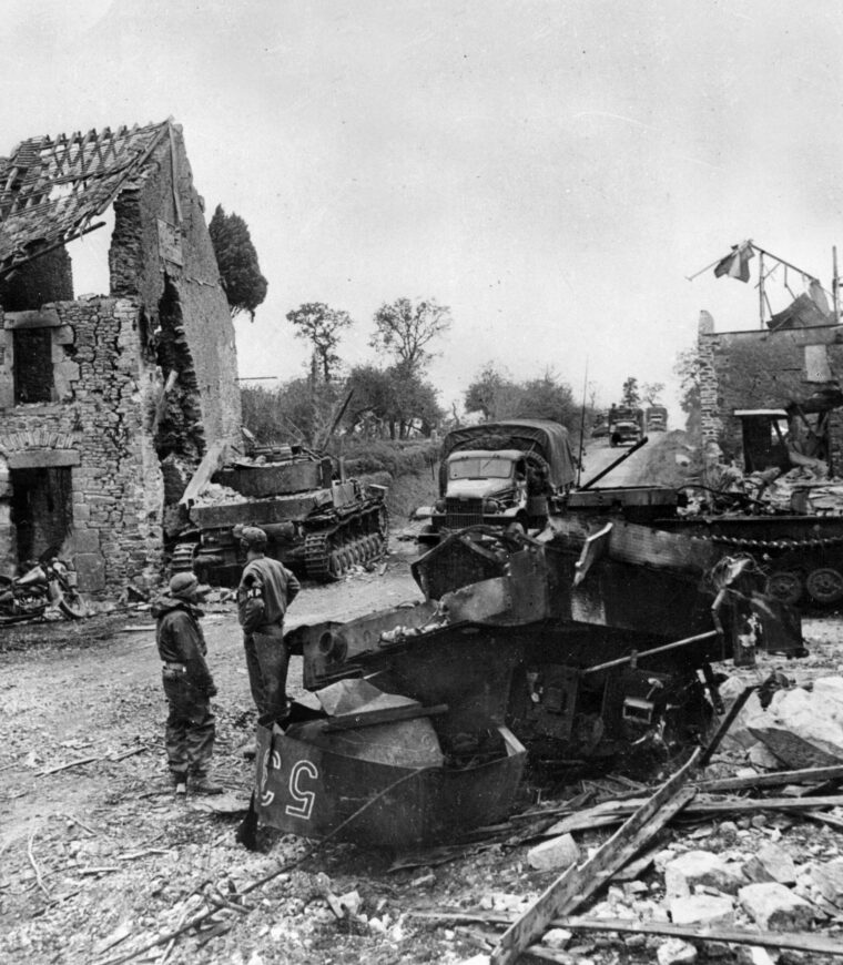 Trucks laden with gas for refueling an advance American tank column enter St. Gilles between two wrecked German tanks. MPs stand by to direct traffic. 