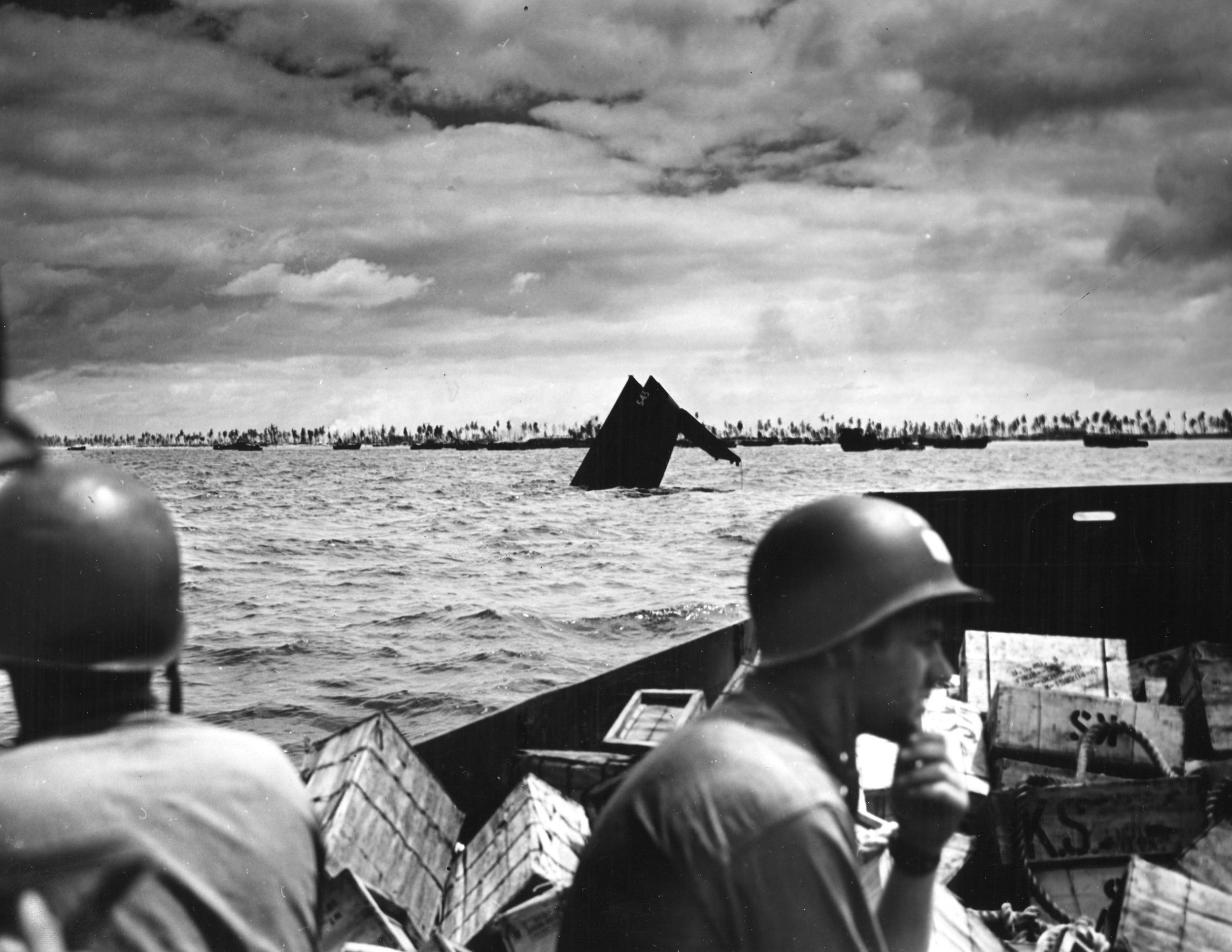 U.S. Coast Guard personnel pass the protruding hull of a sunken American light tanker as they bring supplies to the Betio beachhead.