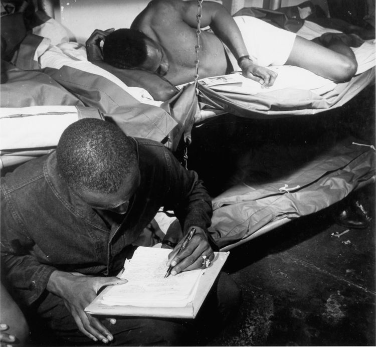 On the eve of the Battle of Manila, one sailor looks at photos of his family while the other writes a letter home, USS Ticonderoga, November 4, 1944. 