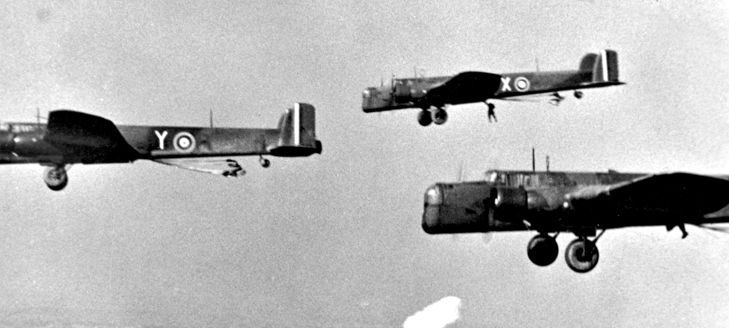 Whitworth Whitley bombers of the Royal Air Force, modified as transport for paras, practice flight operations prior to the Bruneval raid. A para is seen exiting one of the planes in the distance.