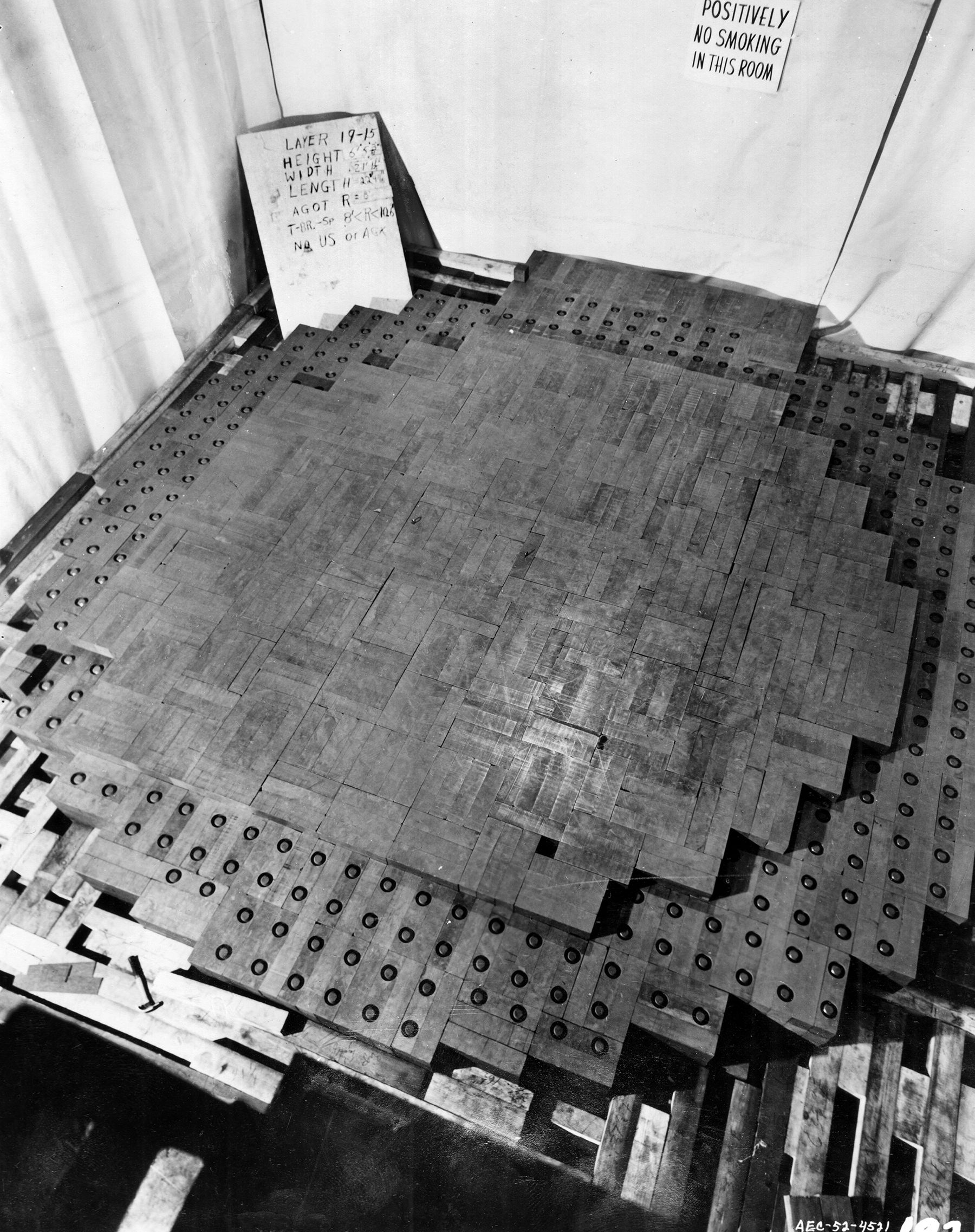 Chicago Pile-1, consisting of blocks of graphite containing uranium oxide, is shown under construction at the University of Chicago. Intended to help prevent the loss of neutrons, the Goodyear balloon cloth draping shown at left and to the rear proved unnecessary during the process that generated the historic nuclear chain reaction.