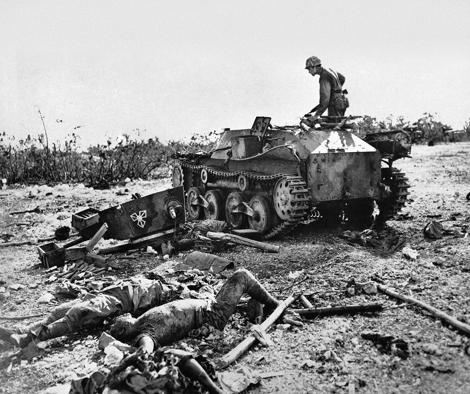 Marine Corporal Edward E. Brooks of Washington, standing atop a Japanese tank he put out of action, looks at the bodies of Japanese tankmen scattered around near the captured Japanese airfield.