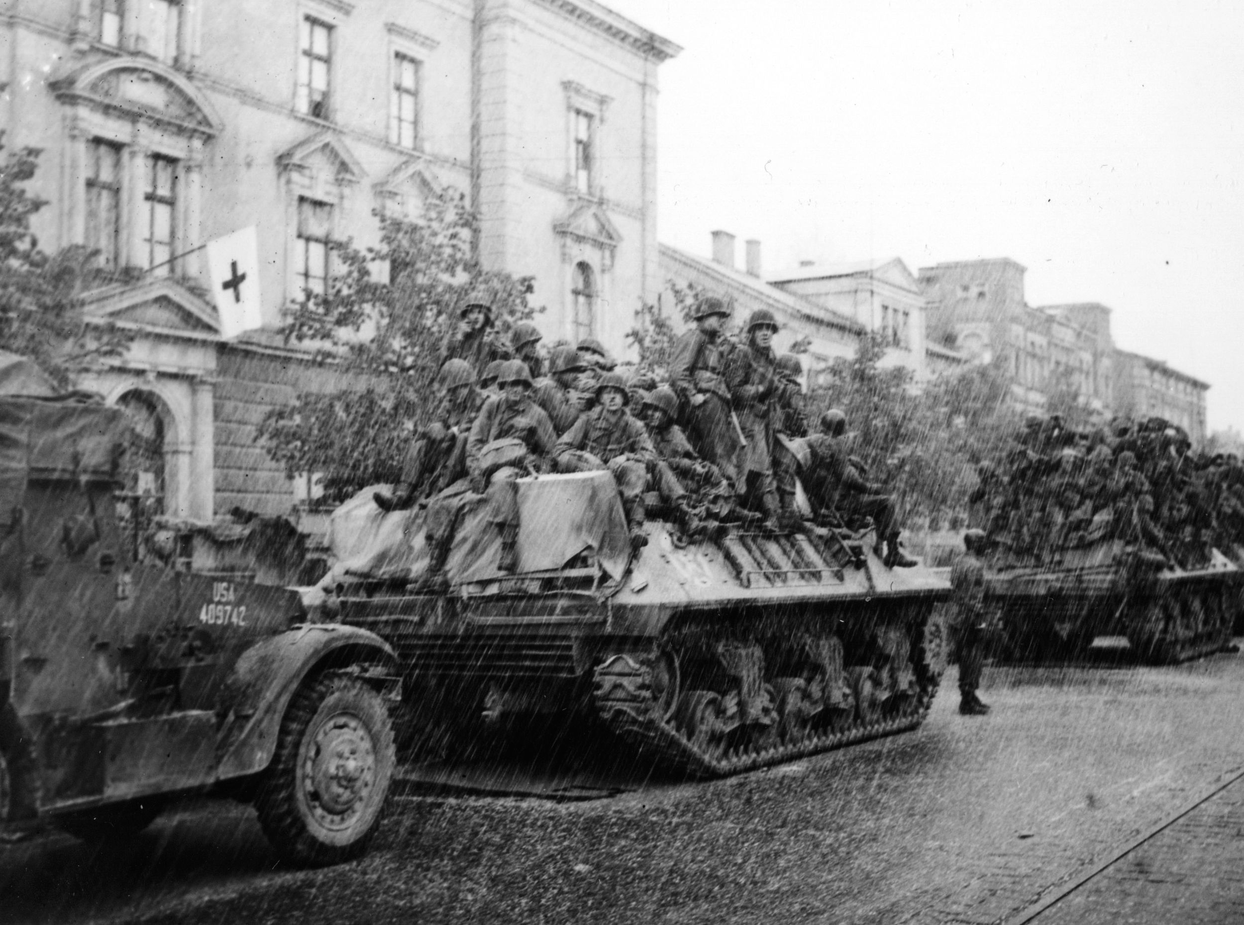 Enduring a storm of hail instead of bullets, 3rd Division infantrymen ride atop Sherman tanks past a hospital in the Bavarian city of Augsburg, Germany, April 1945.