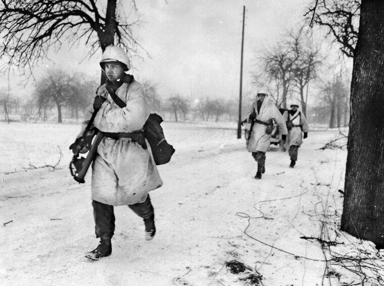 Dressed in white camouflage uniforms, men of the 15th Infantry Regiment advance along a snowy road near Colmar, France, December 1944.