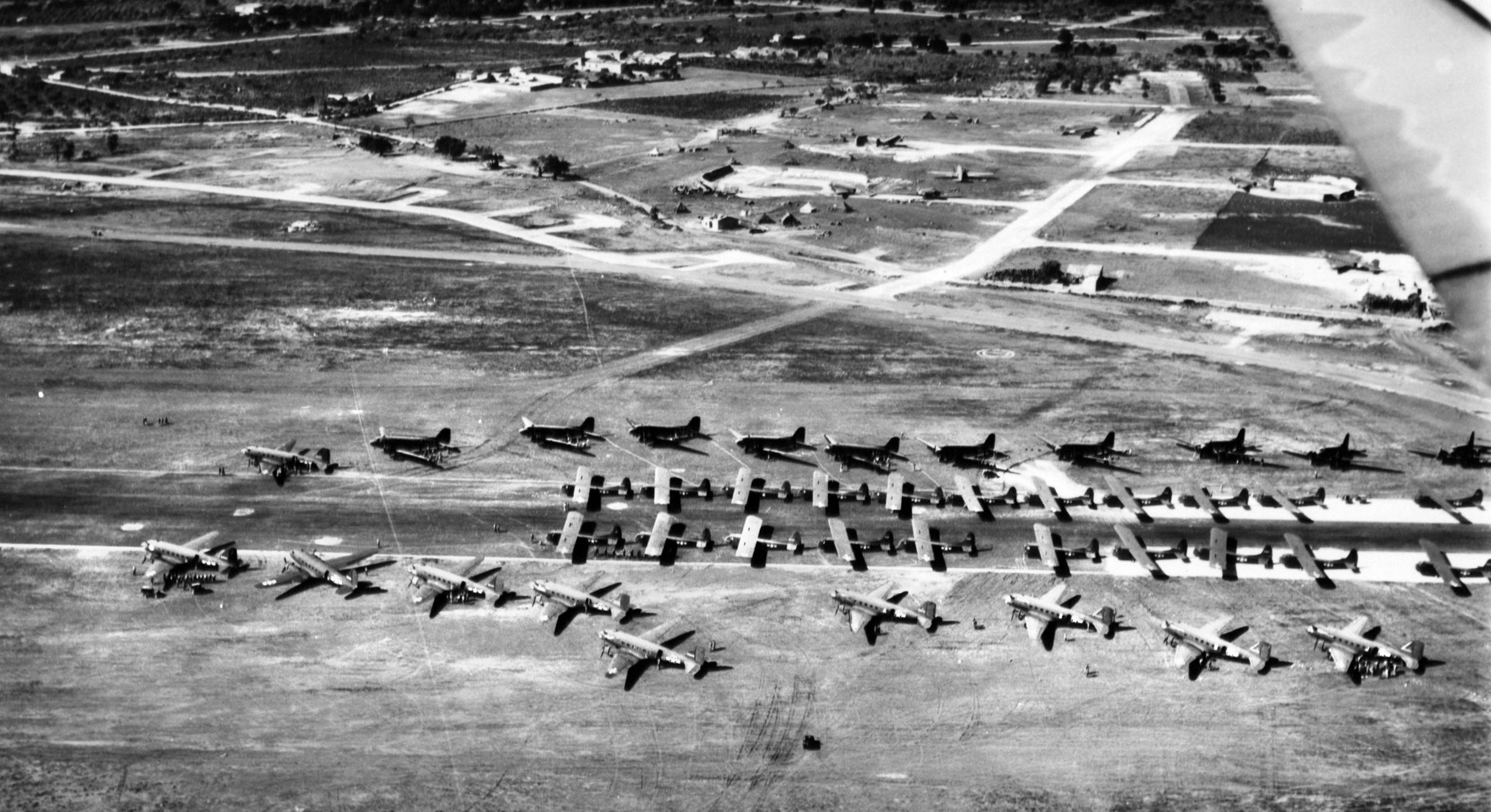 Gliders on the runway, attached to their C-47 tow planes on their flanks, prepare to take off for the invasion of Sicily.