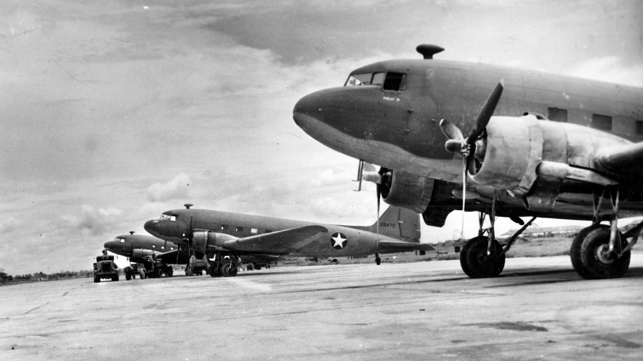 Douglas DC-3 ships standing on the runway at Sookerating Air Base in India. Every ship has a schedule which keeps it in the air the maximum number of hours. The planes that fly over the “Hump”are unloaded a few minutes after landing and take off again for another trip. If possible, each plane must make three trips over the “Hump” each day.