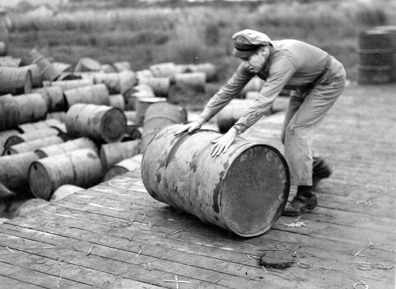 Major Louis E. Scherck, Houston, Texas, 40th Bomb Group, XX Bomber Command in China, “pitches in” and rolls empty gasoline drums to trucks waiting to haul them to another area.