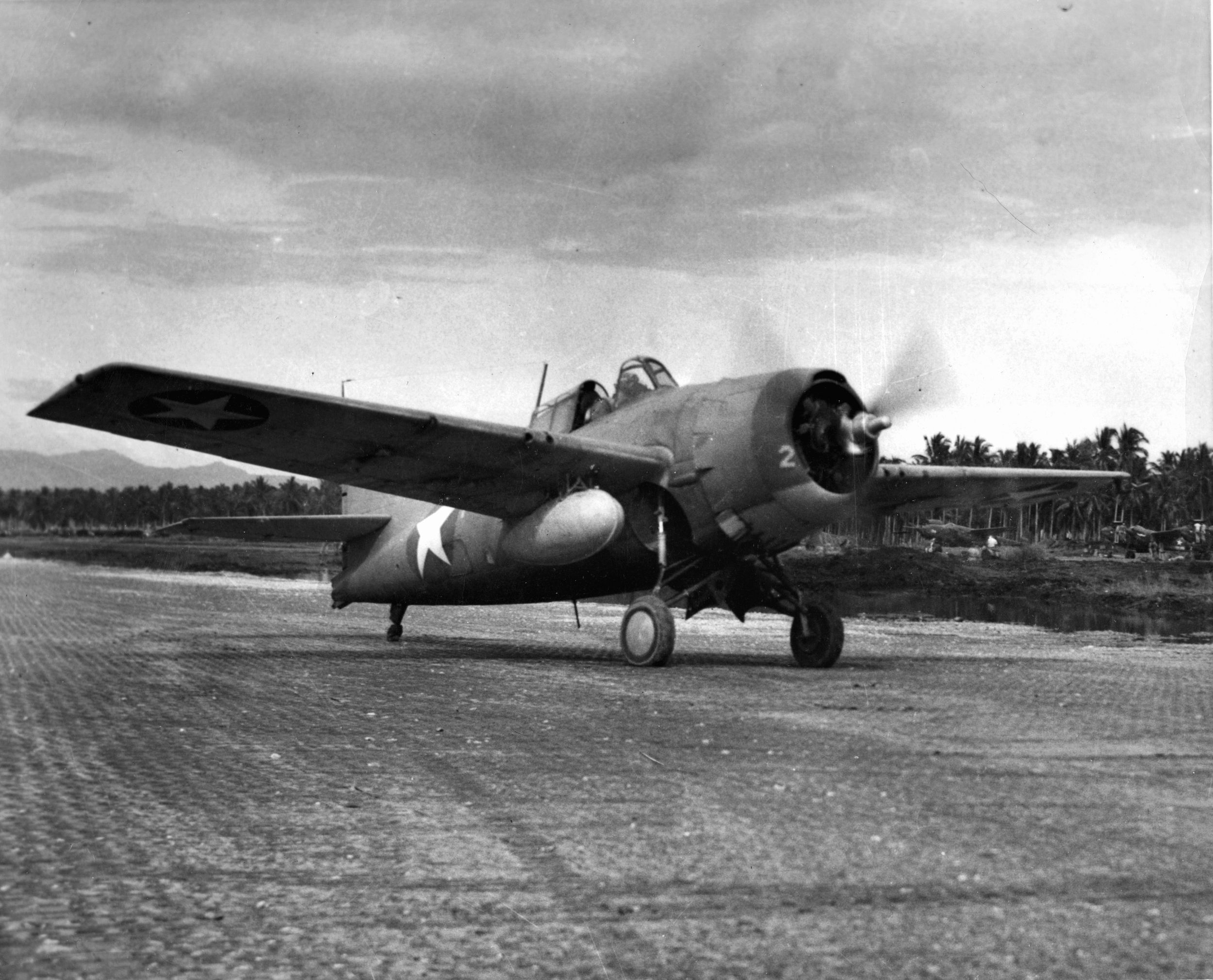 Taxiing on the runway at Henderson Field on Guadalcanal, this Grumman F4F Wildcat fighter has just landed after arriving from an aircraft carrier. The external fuel tank attached to the right wing extended the fighter’s range.