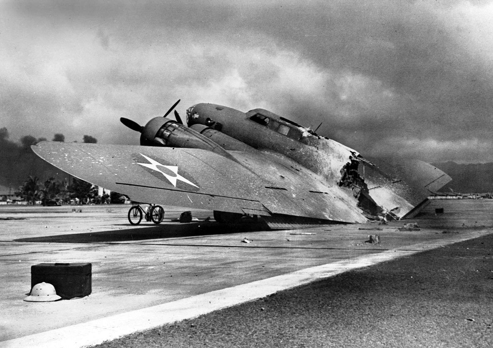 The wrecked U.S. Army Air Force B-17C bomber piloted by Captain Raymond T. Swenson lies on the runway at Hickam Field. Rounds from a Mitsubishi Zero fighter ignited a locker full of magnesium flares that caused the burning bomber to break in half as it landed.