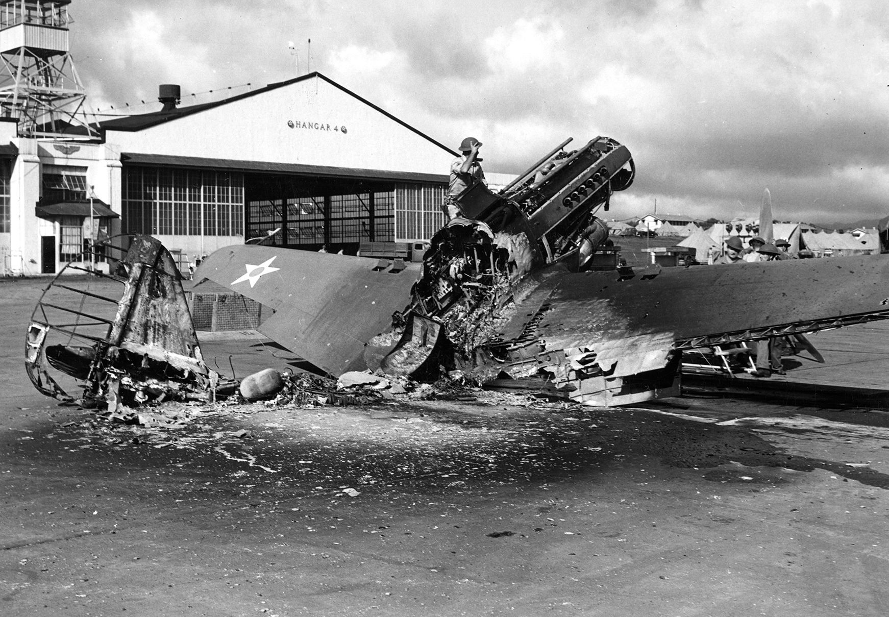 In the aftermath of the Pearl Harbor raid, soldiers examine the charred remains of a Curtiss P-40 Tomahawk fighter plane destroyed on the ground near Hangar 4 at Wheeler Airfield. Many American aircraft were shot to pieces by strafing Japanese planes on December 7, 1941. 