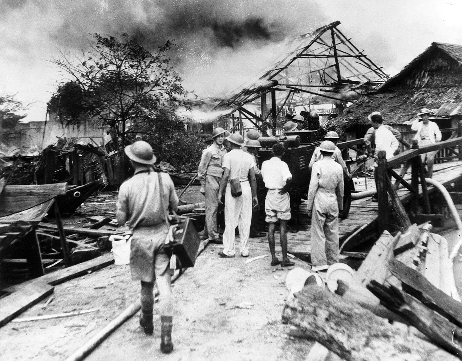 Australian soldiers, exhausted and stunned by the ferocity of the Japanese onslaught in Malaya, watch the destruction of an enemy air raid against Singapore unfold before their eyes in February 1942. 