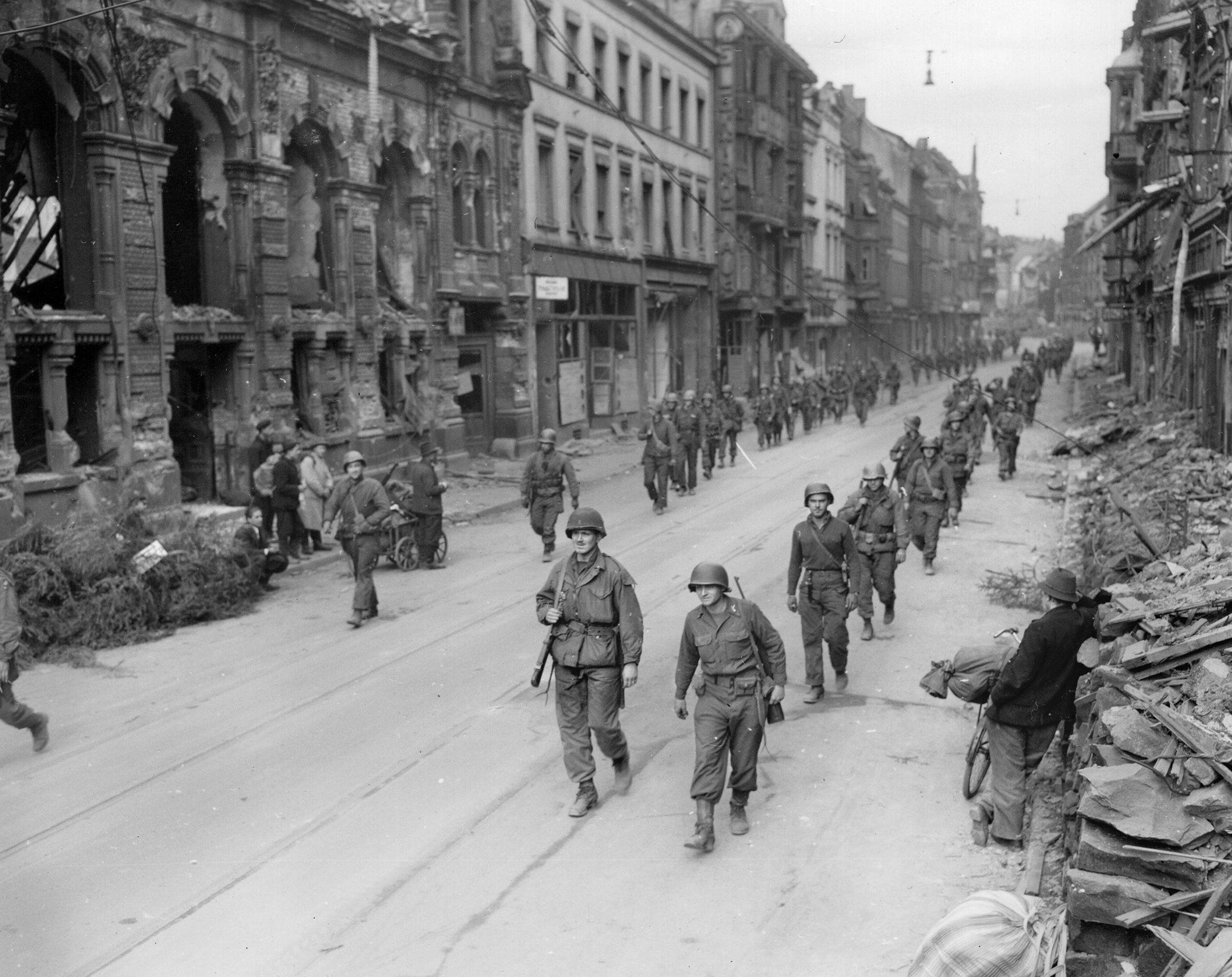 Men of the 2nd Battalion, 275th Infantry, 70th Division, move through Saarbrücken while being watched by citizens, March 20, 1945.