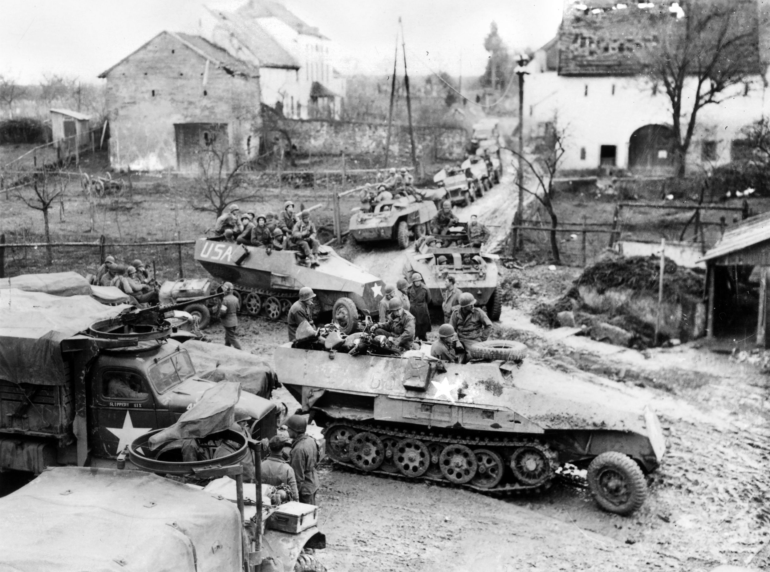 With several men in a captured German halftrack leading a column of vehicles, troops of the 5th U.S. Infantry Division wait for orders to move out from a Belgian village toward the Rhine River. The “Red Diamond” division would cross at Oppenheim on the night of March 22, 1945.