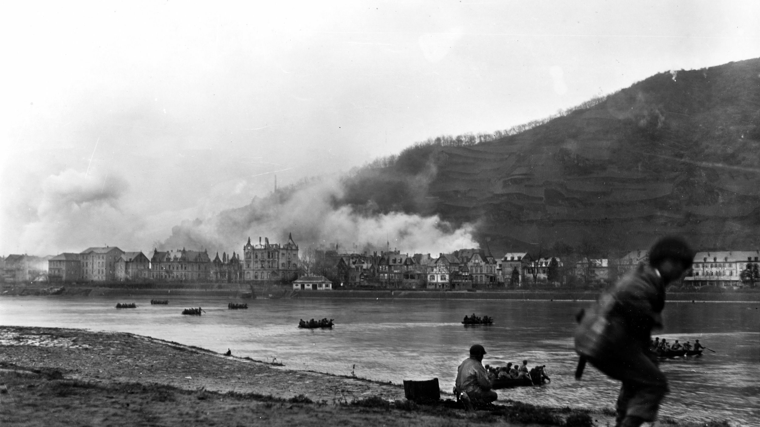 Assault boats carry Patton’s Third Army troops across the Rhine at St. Goar, Germany. Troops in foreground are on the alert for snipers.