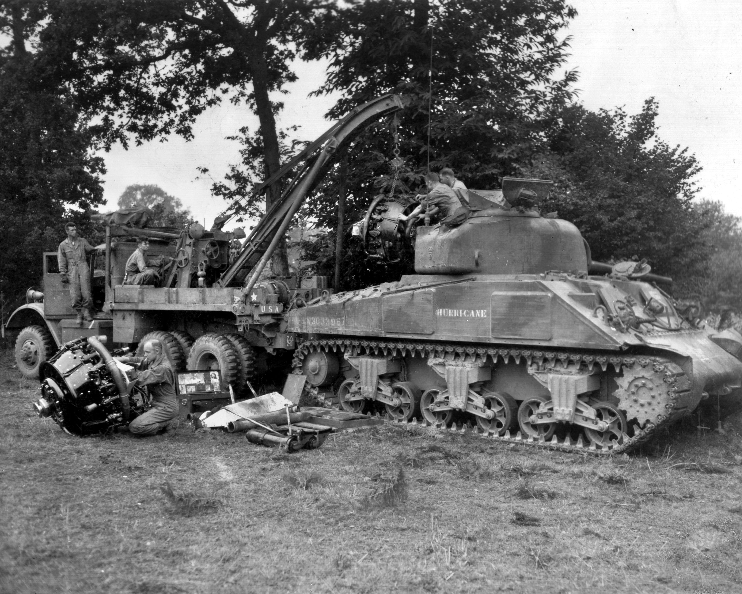 Using a Federal C-2 wrecker, a maintenance crew installs a new radial airplane engine in a 2nd Armored Division Sherman tank named “Hurricane” near the front lines at Le Teilleul, France, east of Avranches, July 1944.