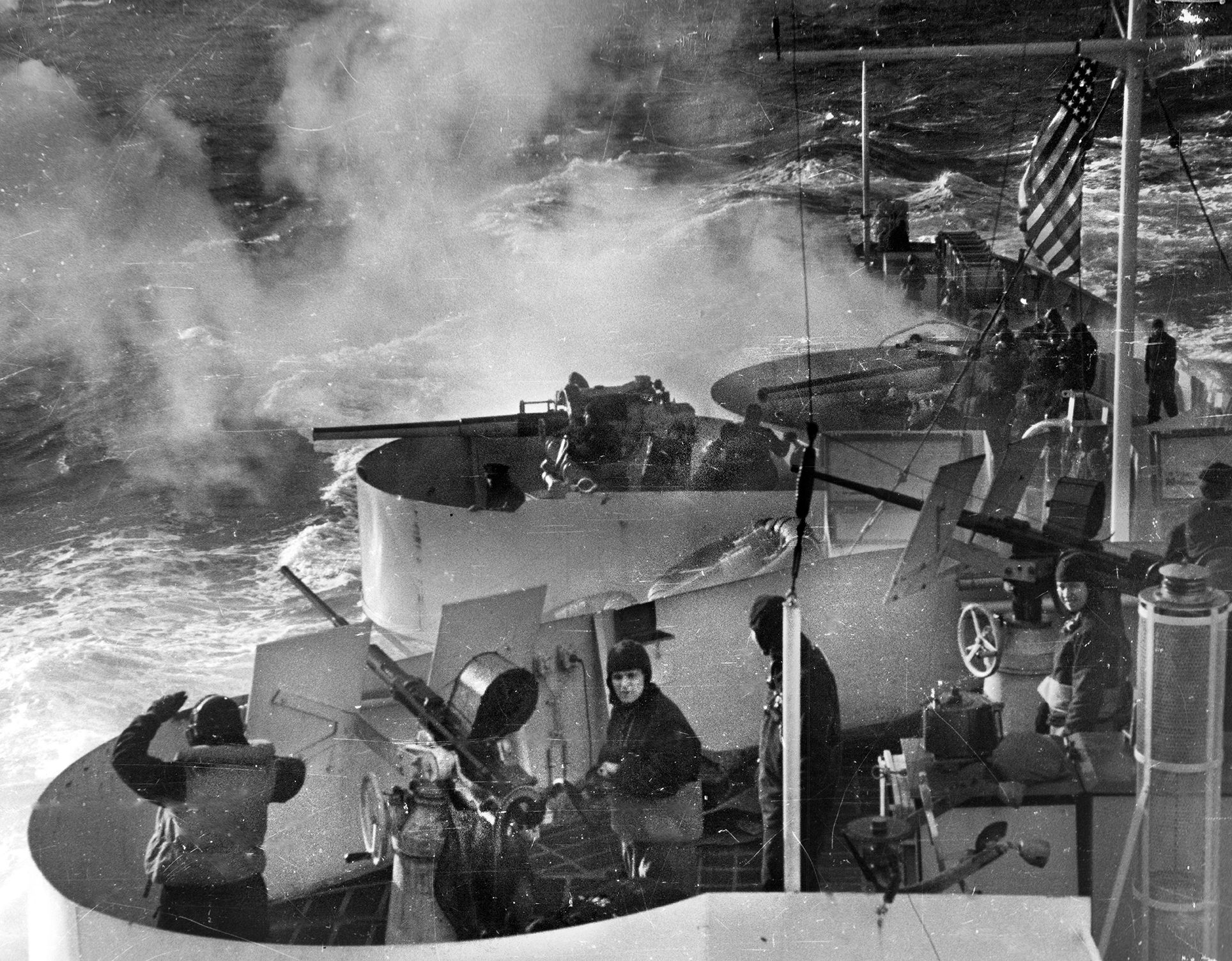 Manning their battle stations during an exercise, Coast Guardsmen aboard a cutter at sea await orders to open fire with their guns.