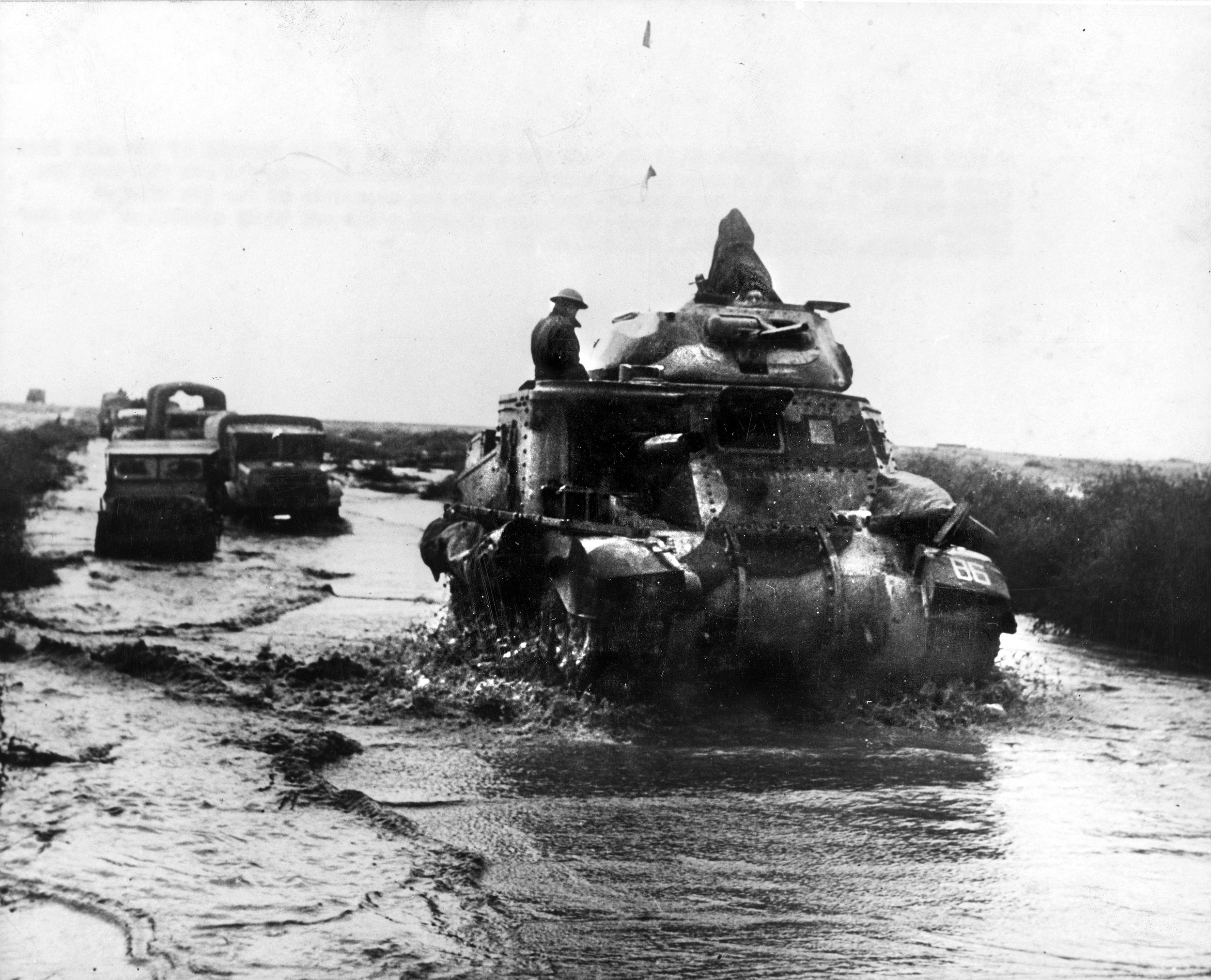 During fighting in North Africa, British troops ride through heavy rain and mud across the Libyan landscape. Their Grant tank mounts a 37mm gun in a small turret and a sponson mounted 75mm gun.