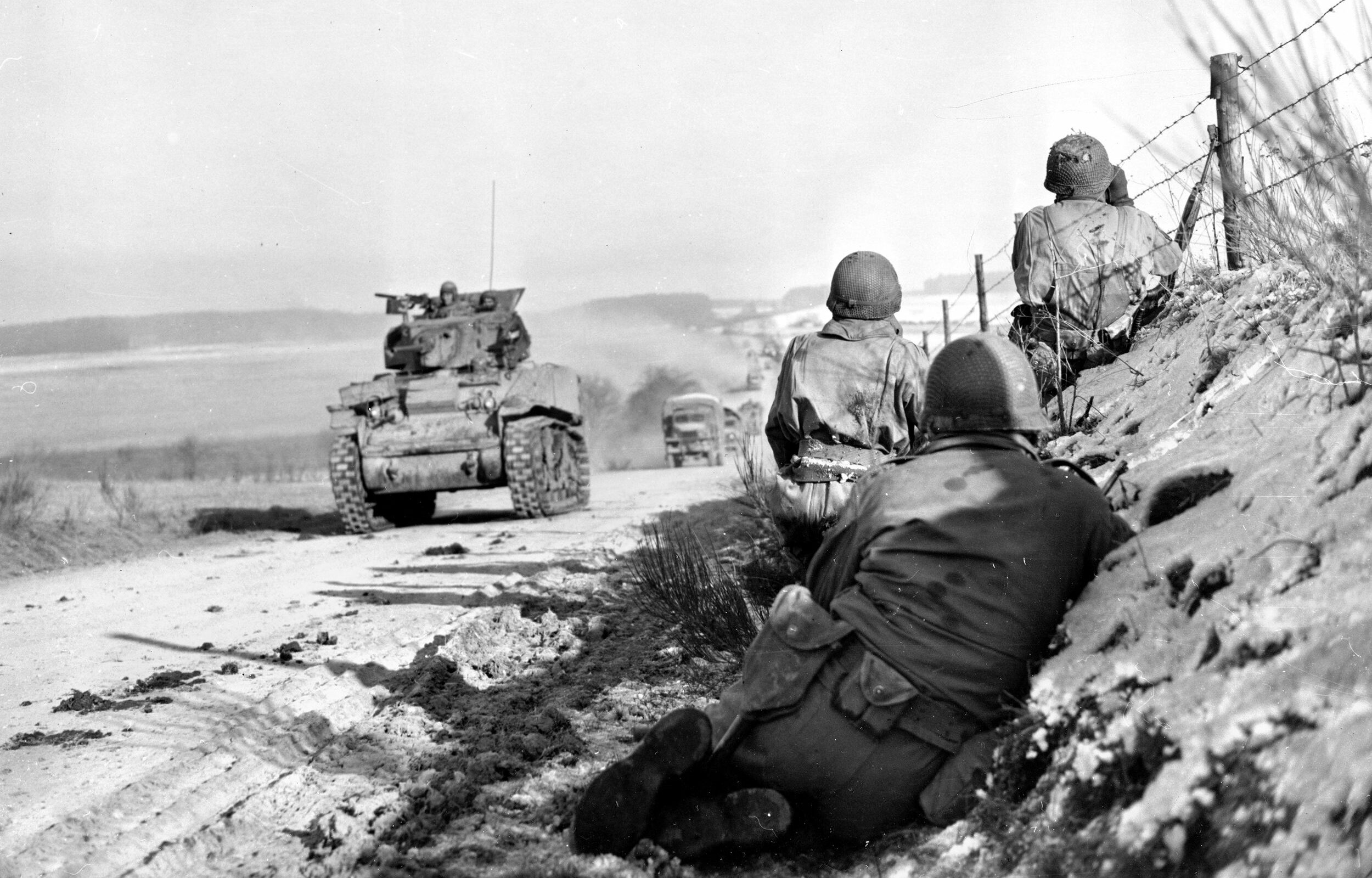 Infantrymen of the 4th Armored Division protect the flanks of a column of M4 Sherman medium tanks proceeding down a road toward Bastogne. German infantrymen were sometimes seen to emerge from cover and fire the Panzerfaust anti-tank weapon at American armored vehicle.