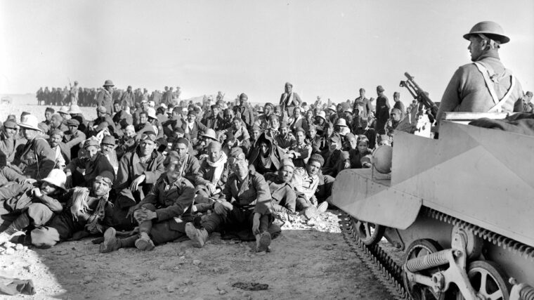Captured Italian soldiers sit under the watchful eyes of a British soldier perched aboard a Bren Gun carrier on December 16, 1940. These men were captured during the British offensive in the Western Desert that inflicted a stinging defeat on Italian forces.