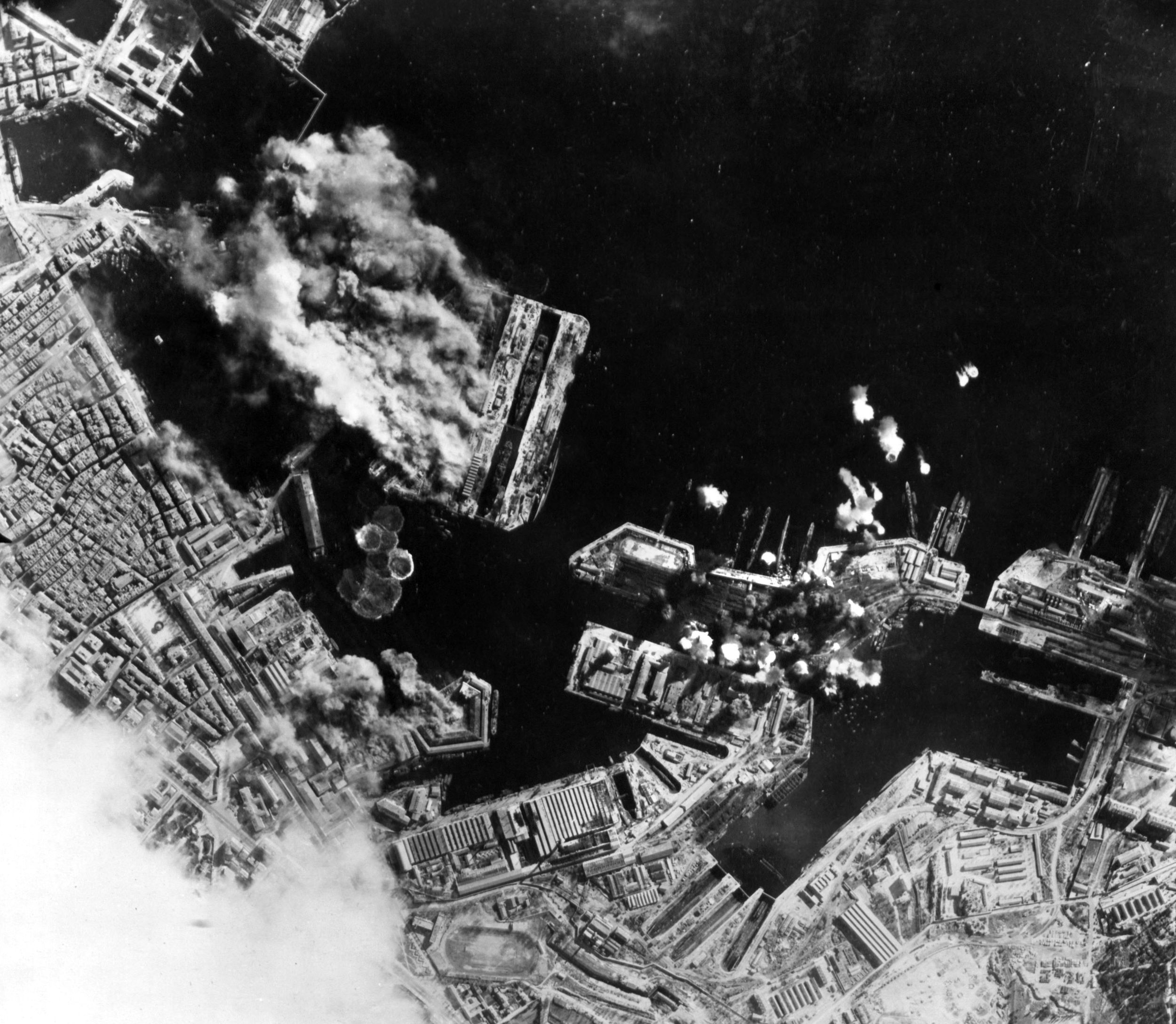On February 4, 1944, Allied bombers of the U.S. Fifteenth Air Force struck the Nazi submarine base at Toulon in occupied France. Weather reports from Detachment G were critical to the success of the raid. This image shows the opening moments of the air assault as warehouses, a drydock, and other installations are seen being pounded by bombs.