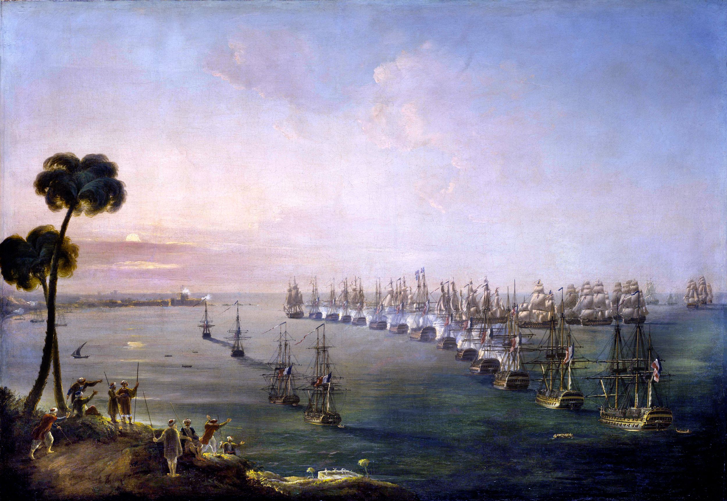 The beginning of the Battle of Nile, at sunset. Nelson’s fleet, led by HMS Goliath, is shown at the head of the anchored French line, with the Aboukir fort, in the background at left. The brunt of the British ship attack is from the seaward side, but  the Zealous can be seen rounding the bow of the French Guerrier, at the head of the French line, to lead an attack from the landward side. At right is the rearmost of the anchored French ships of the line, the Timoleon.  Painting by Nicholas Pocock, 1808.