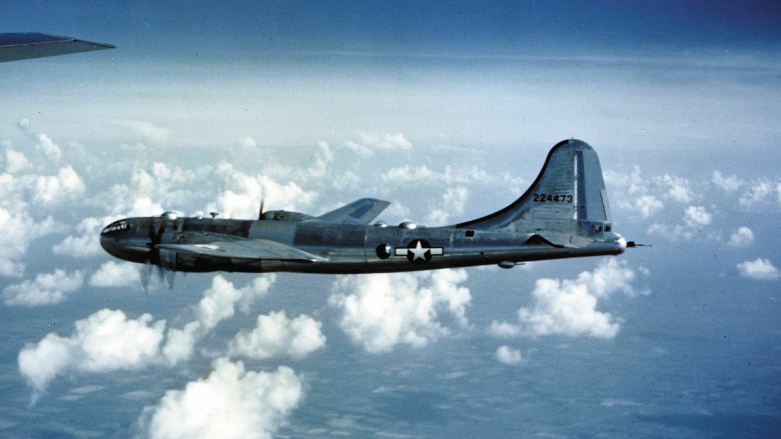 High above the clouds, a four-engine Boeing B-29 Superfortress heavy bomber wings its way toward a target in Japan.