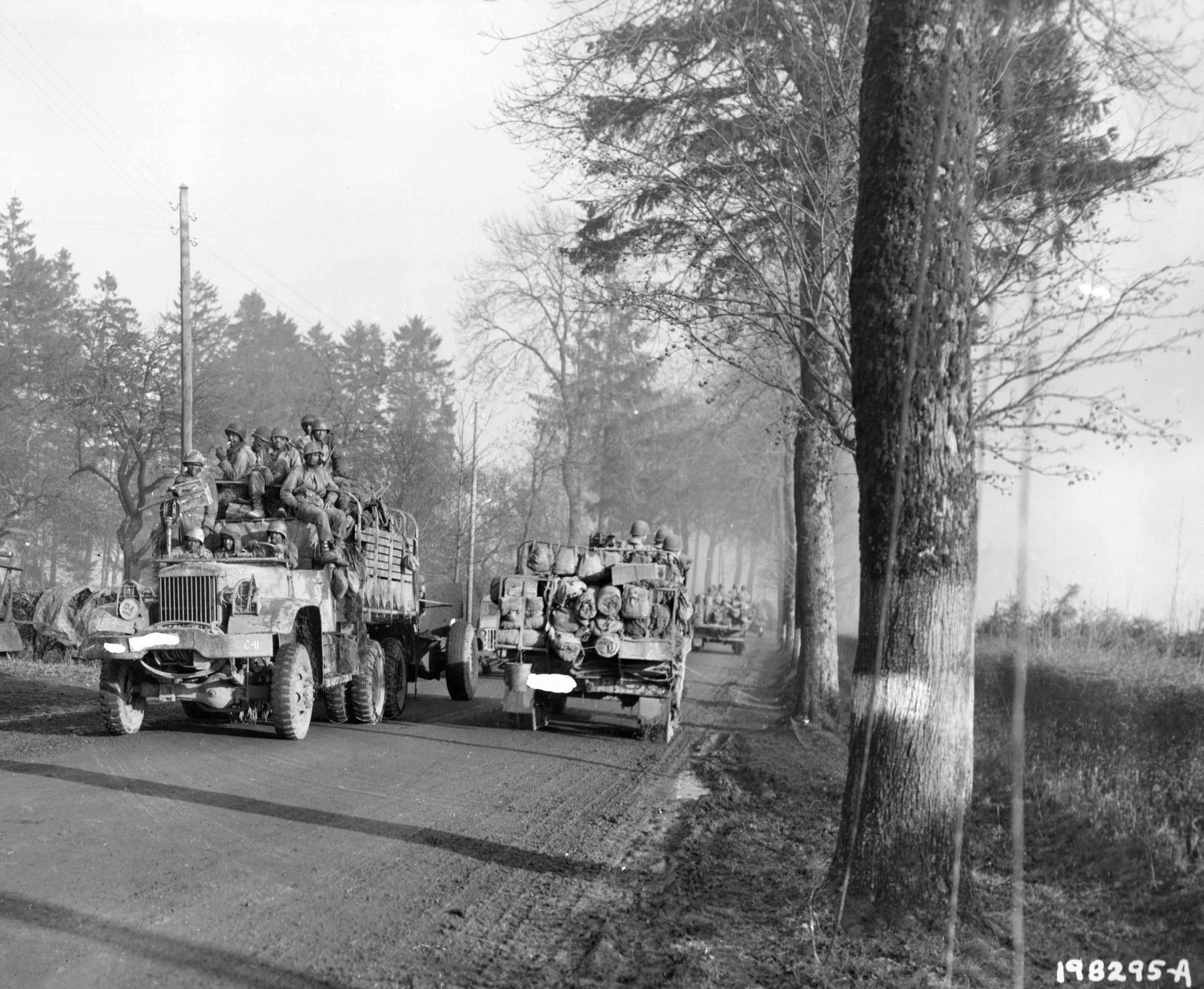 African-American soldiers of a field artillery unit, one of four engaged in support of the defenses at Bastogne, relocate to a new position at left as another truck carries troops and equipment forward. This photo was taken on December 20, 1944.