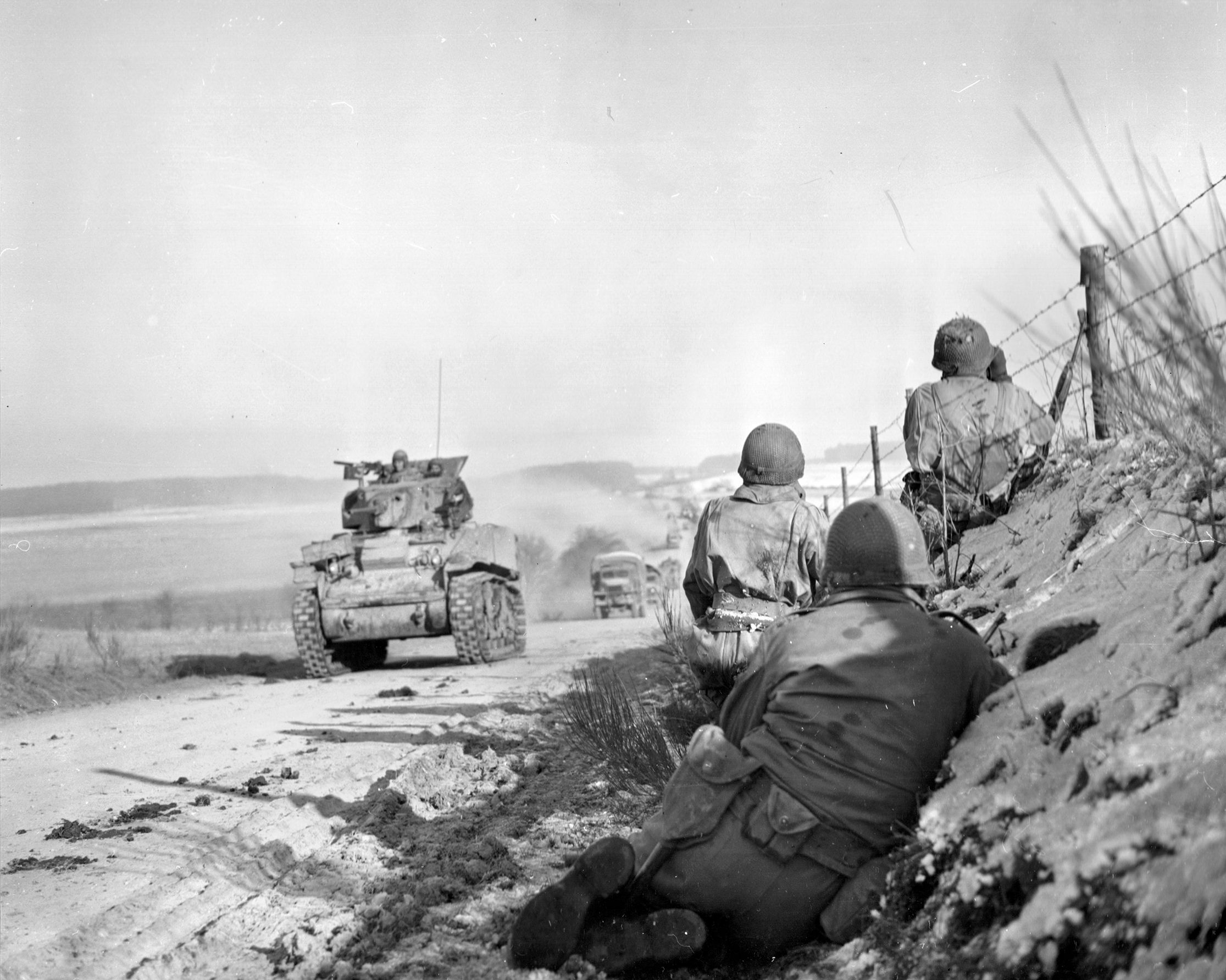 Working in mutual support, M4 Sherman medium tanks of the U.S. 4th Armored Division make their way toward Bastogne while American infantrymen guard their flanks and watch for signs of enemy activity during the Battle of the Bulge. 