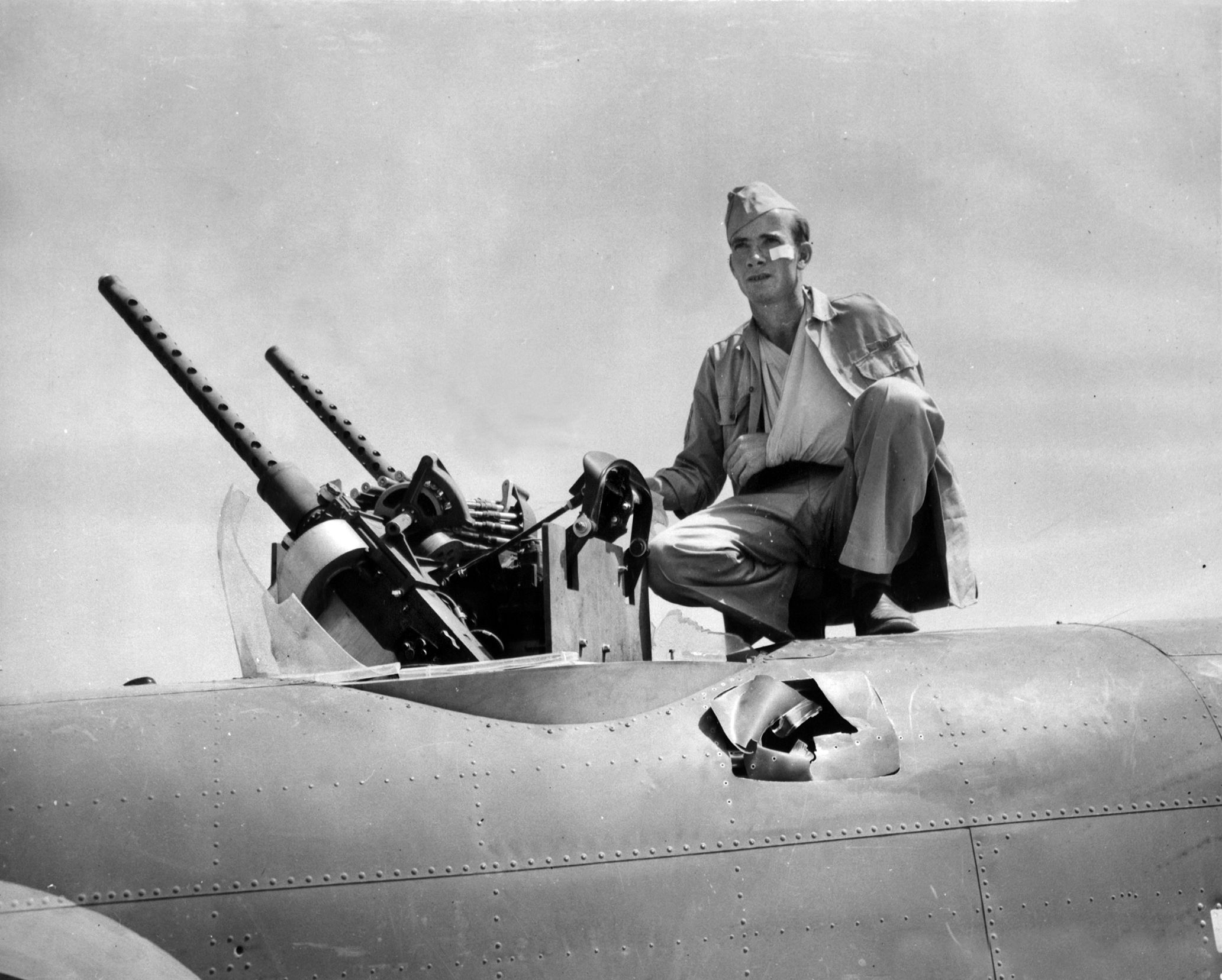 Staff Sergeant Billy Dykes sits near the upper turret of his B-25 bomber at Gerbini airfield, Sicily. German flak damaged the aircraft near his position, and he received minor injuries. Note the point of impact just below his location.