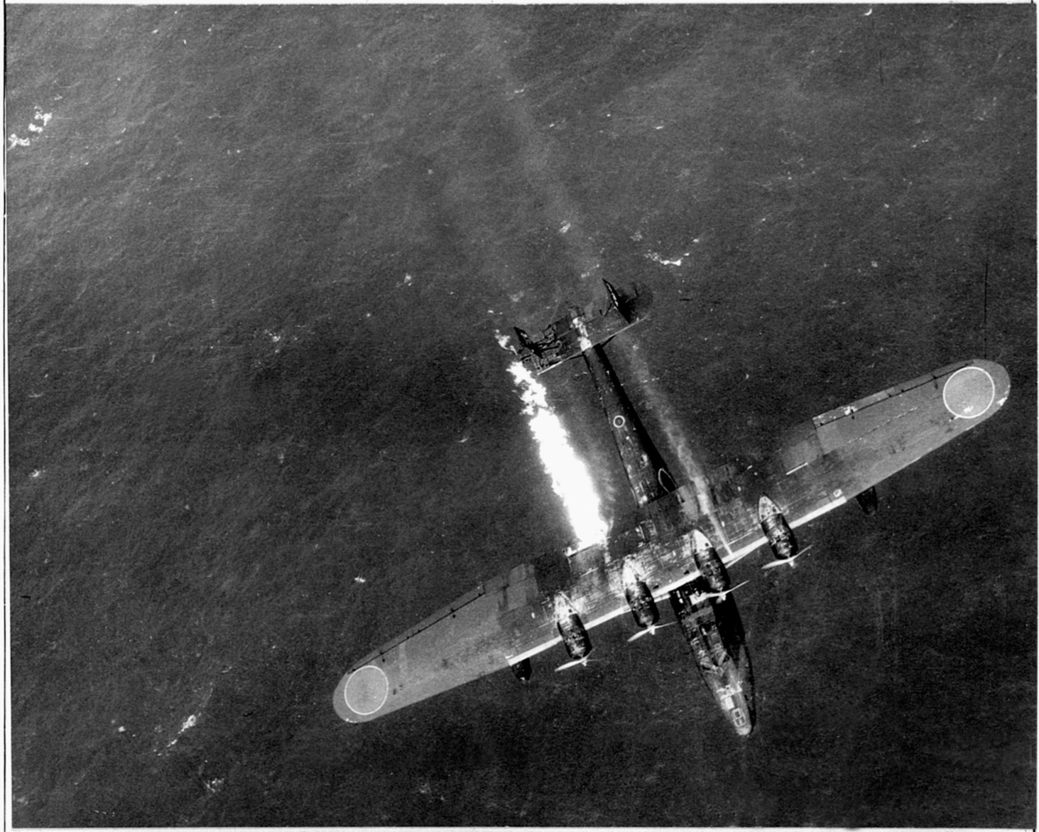 After sustaining damage from heavy fire, a Japanese flying boat—its wing trailing smoke and flames—plummets from the sky.