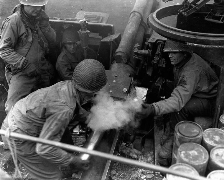 Members of the U.S. 9th Armored Division fire 105mm shells on an enemy target.