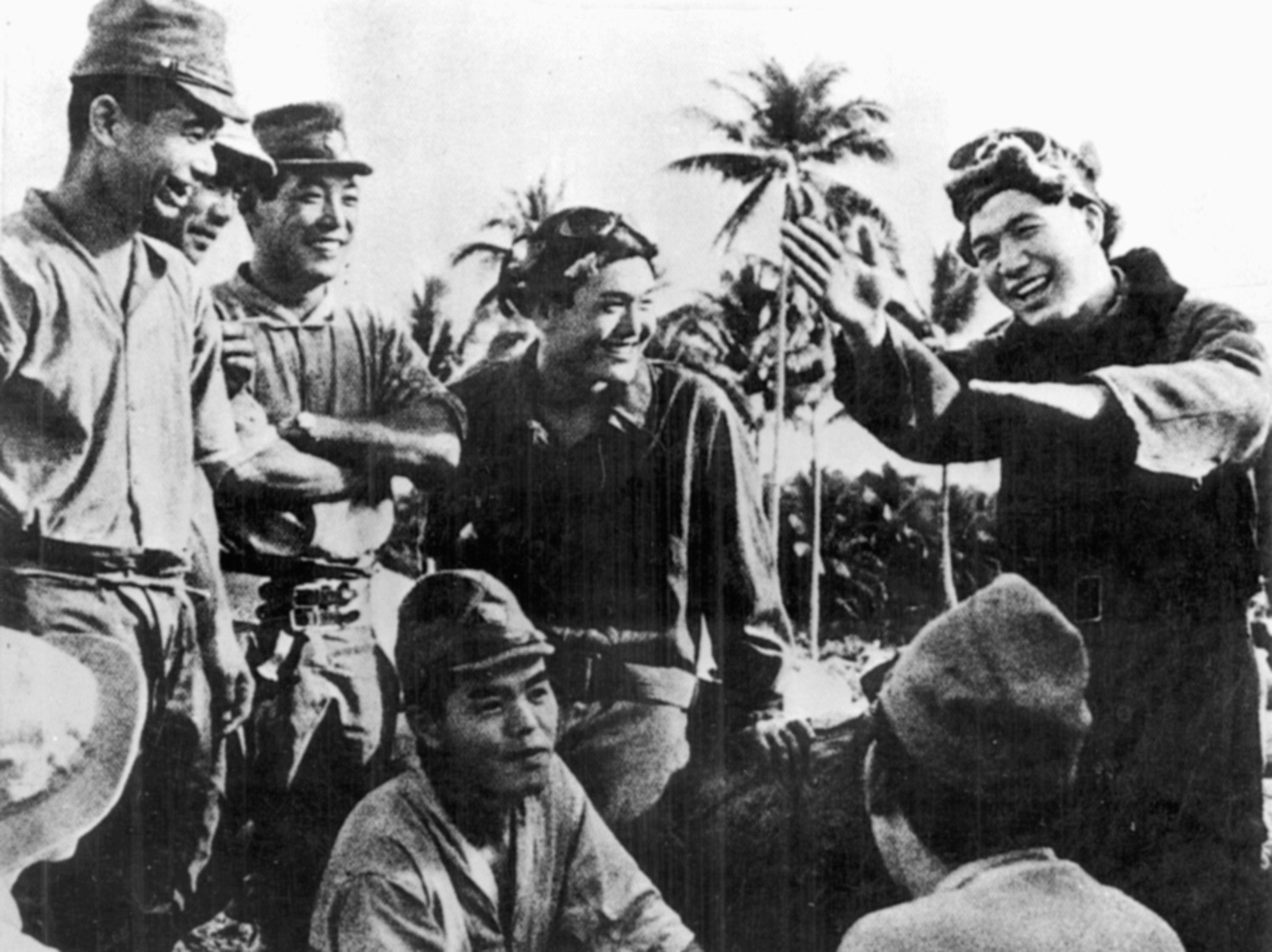Japanese pilots smile as they listen to a comrade recount his experiences of aerial combat over Wake Island.