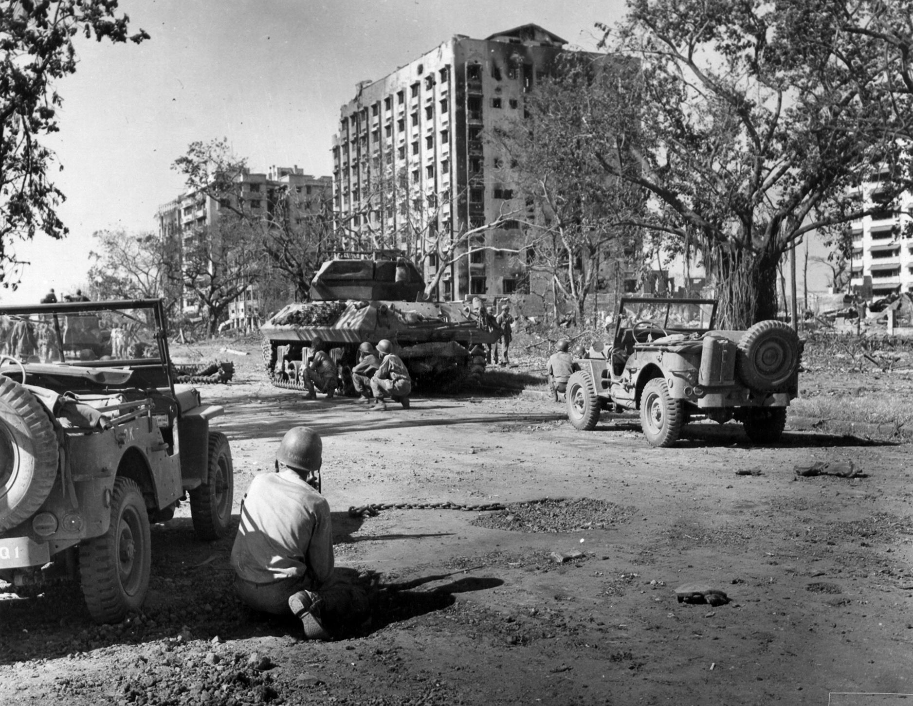 American tanks are poised to enter Manila in this photo taken in March 1945, but their progress is temporarily held up by Japanese sniper and machine-gun fire. American soldiers crouch behind the vehicles, taking cover from the hail of bullets.