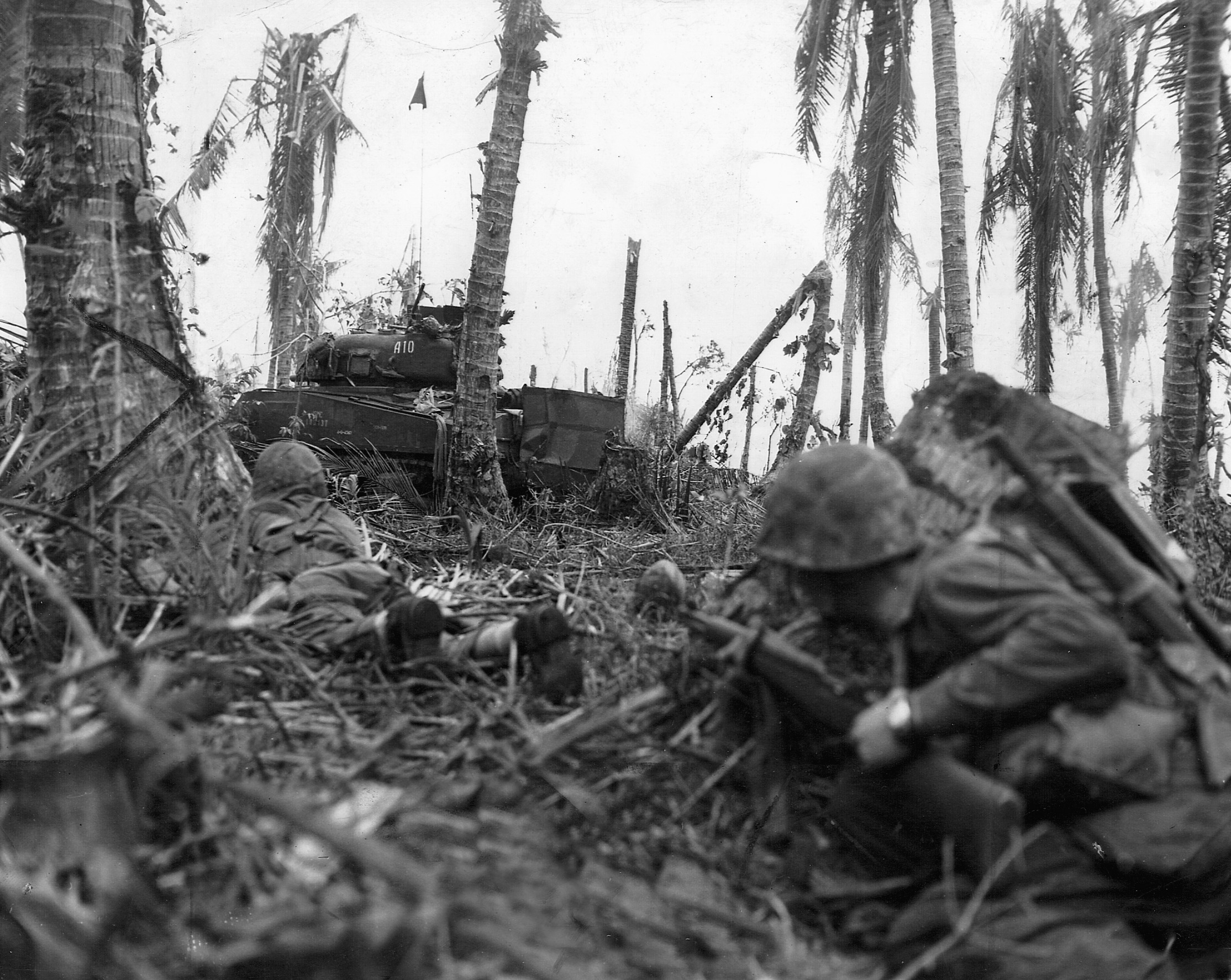 Two Marines crouch low, while cautiously making their way towards a Japanese stronghold.