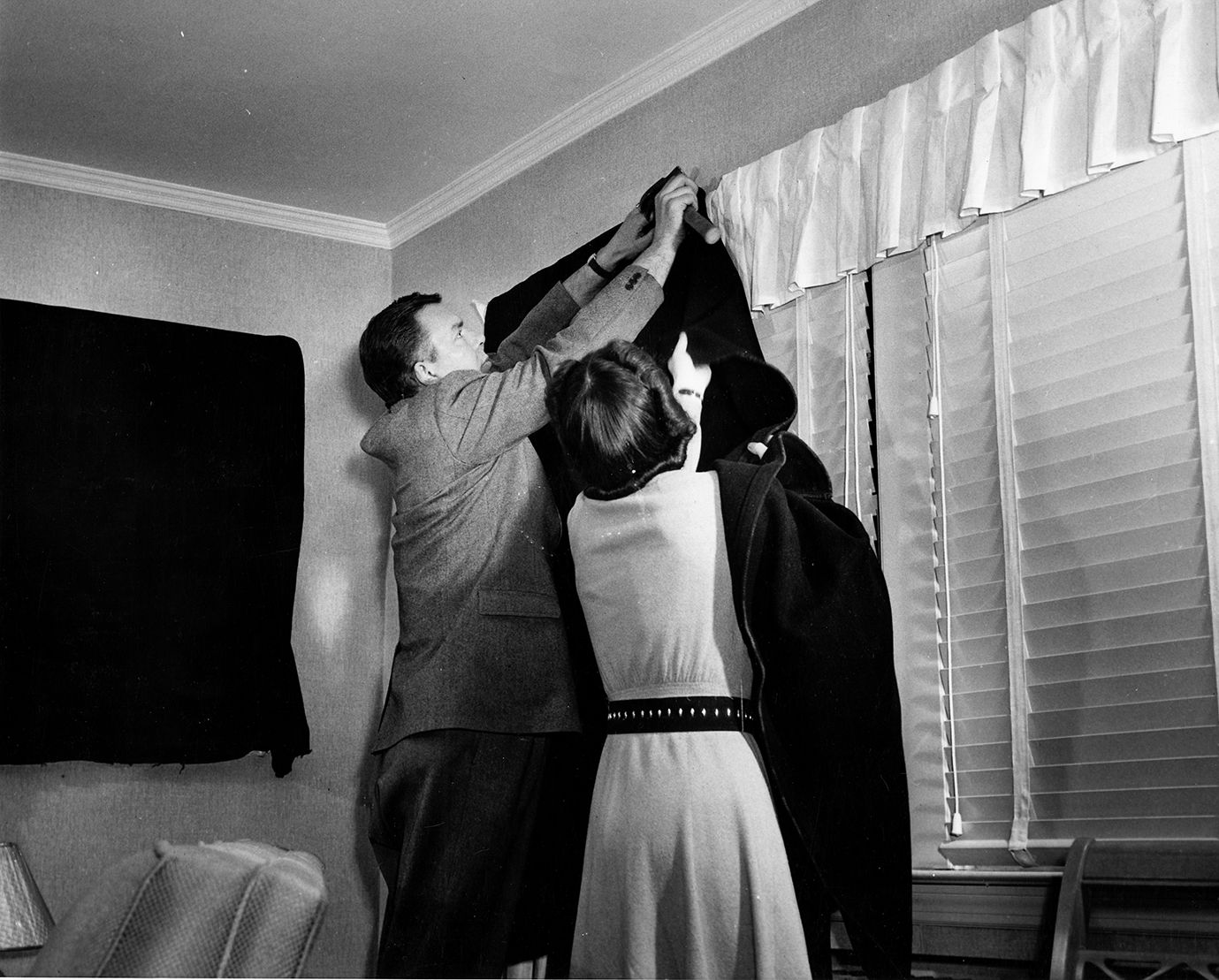 A husband and wife hang black-out fabric over their windows in California, as encouraged by the civil defense sign.
