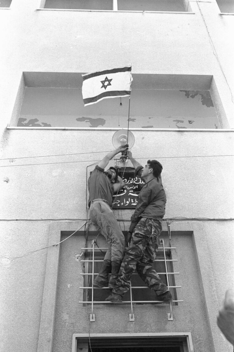 Two Israeli soldiers host their country’s flag on the police station of Jenin. 