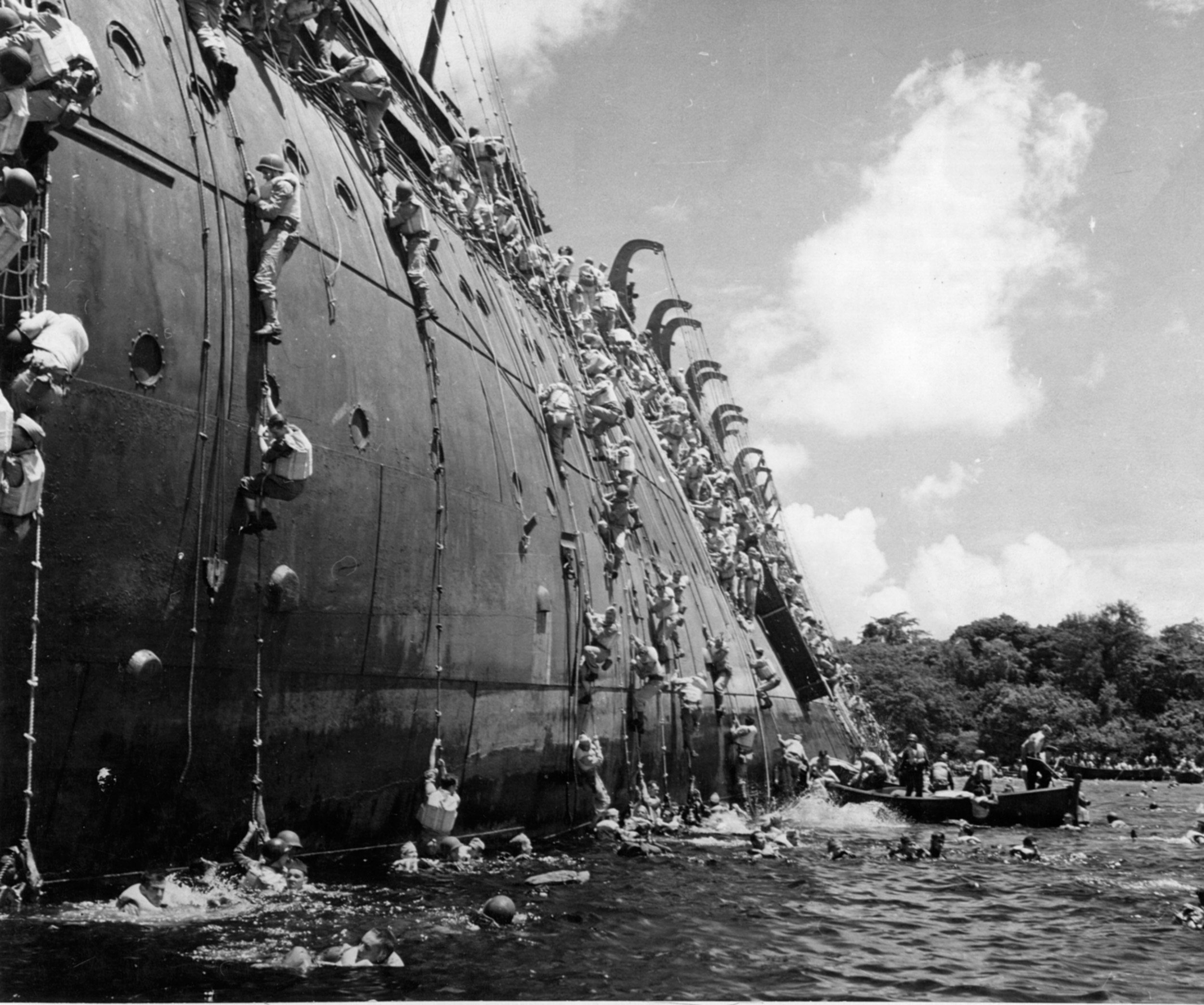 Soldiers scramble down the side of the SS President Coolidge as the ship lists heavily. Life boats await those who cannot swim.