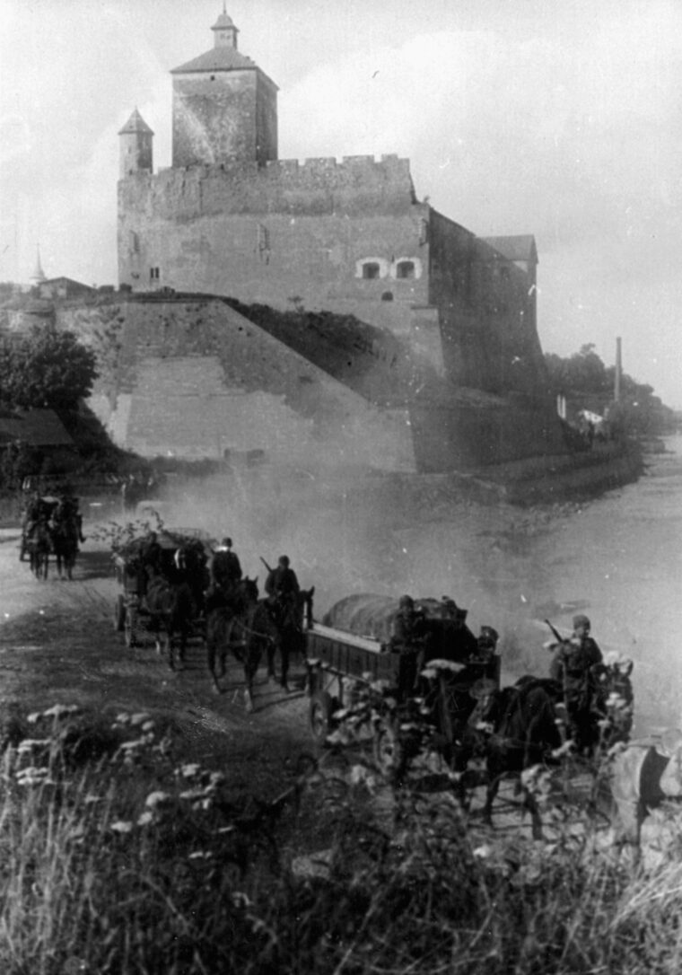 Soviet troops with horse-drawn caissons and wagons advance along a dusty road in the imposing shadow of the Alte Burg am Ufer at Narva.