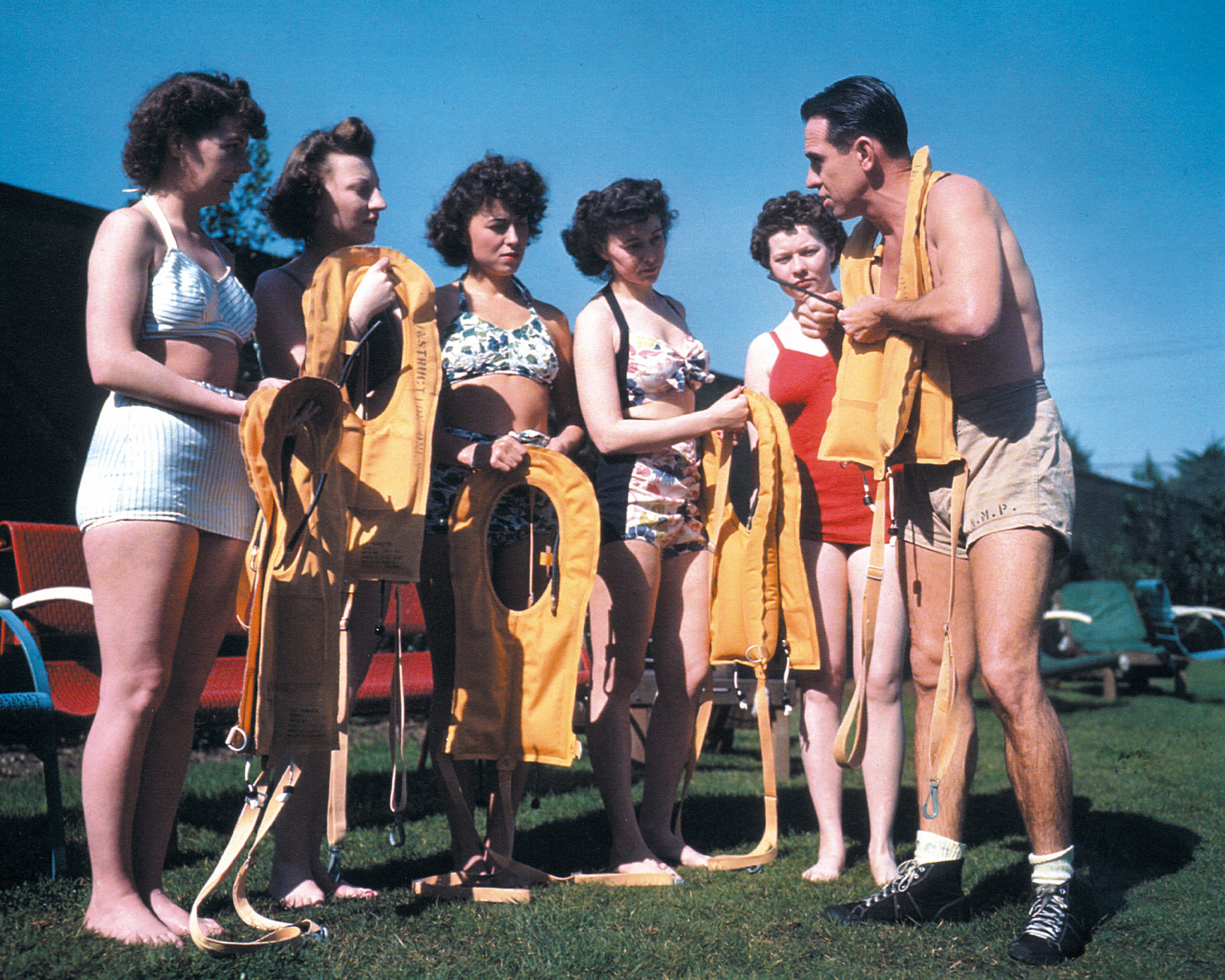 A Navy instructor explains a flotation device to some recruits wearing non-government issue swimsuits during “ditching procedure” training. It is not known whether women referred to the devices as “Mae Wests” as the men did.