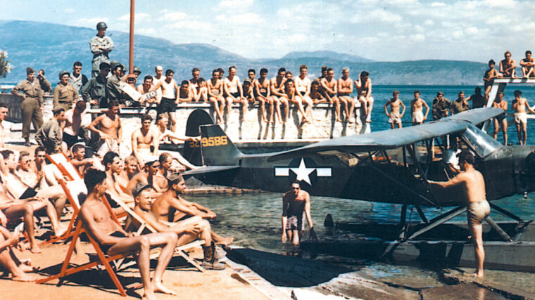 On the coast of Italy, military personnel take time out from their duties at the beach. The water adapted observation plane may have been used for water skiing.
